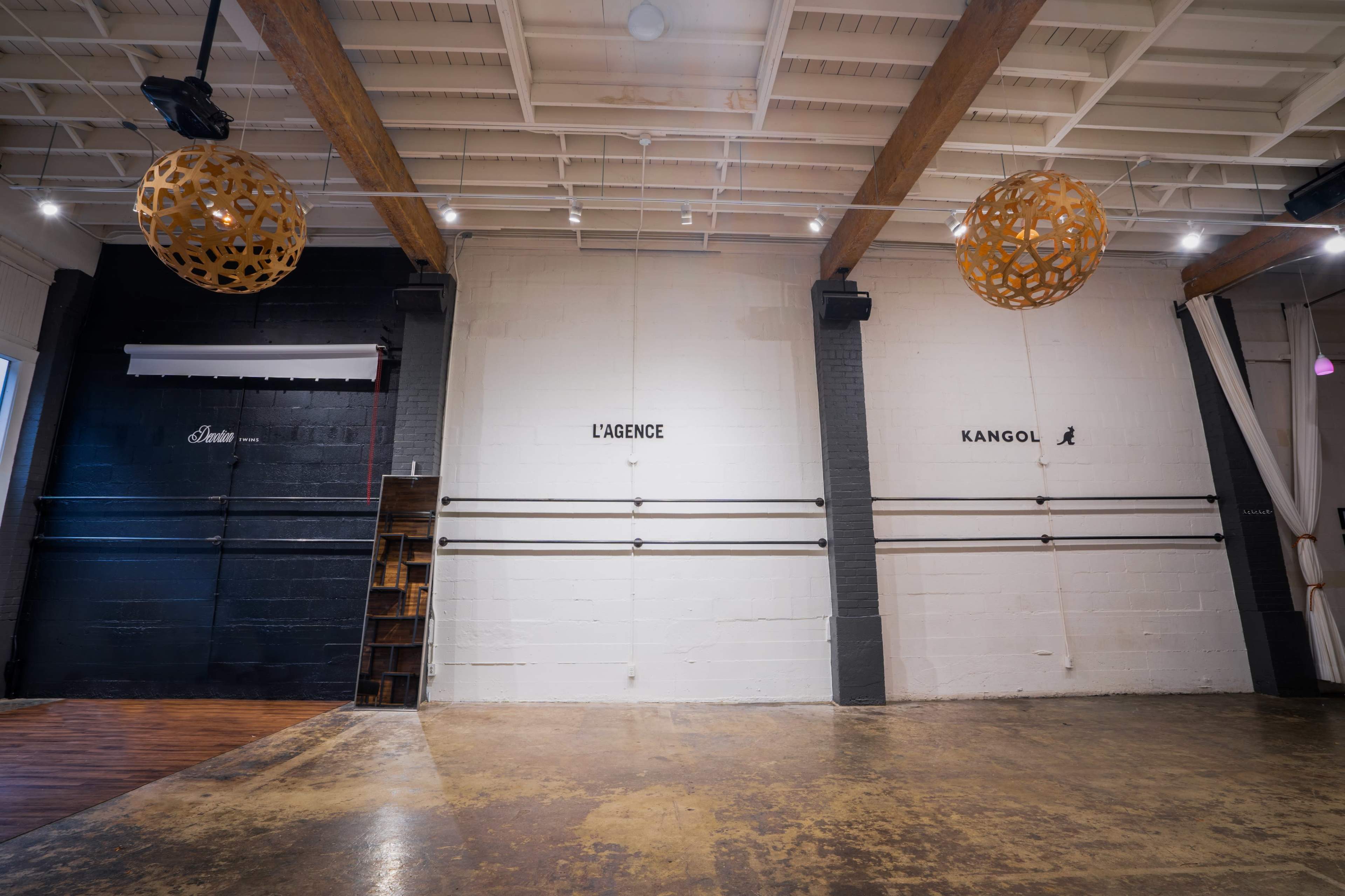 A spacious interior with two prominent walls featuring the words "L'AGENCE" and "KANGOL" painted on them, alongside decorative spherical light fixtures hanging from the ceiling.