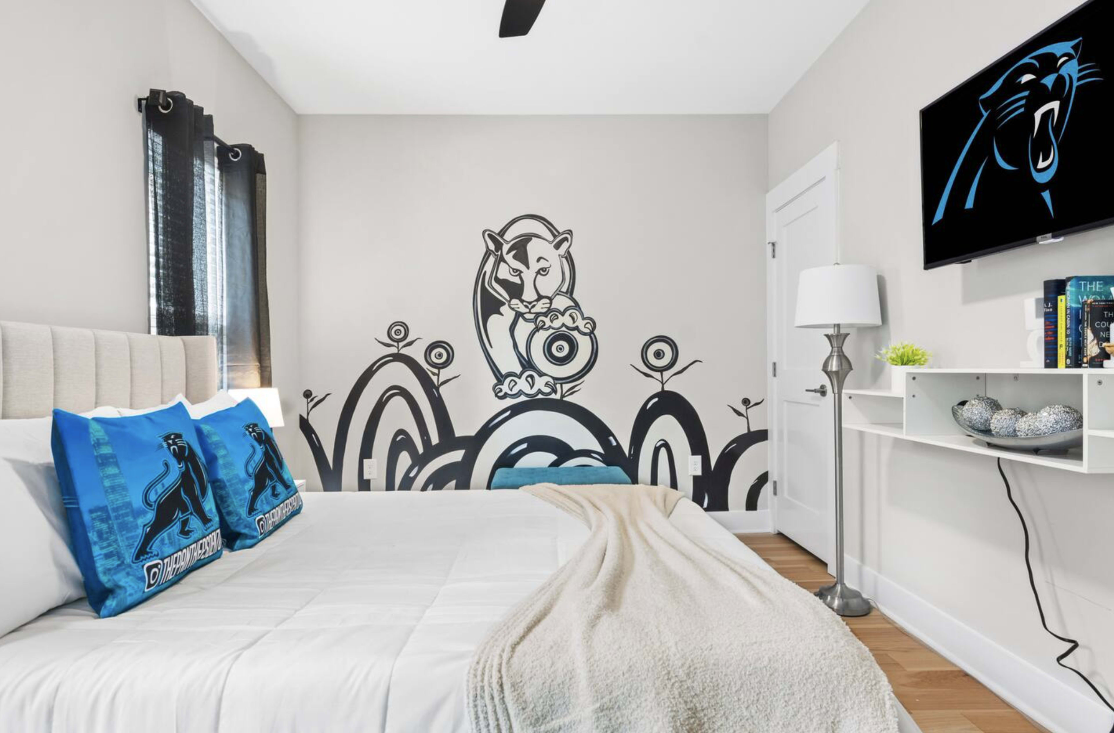 The bedroom features a bed with blue decorative pillows, a large wall mural of a panther, and a TV mounted on the wall.