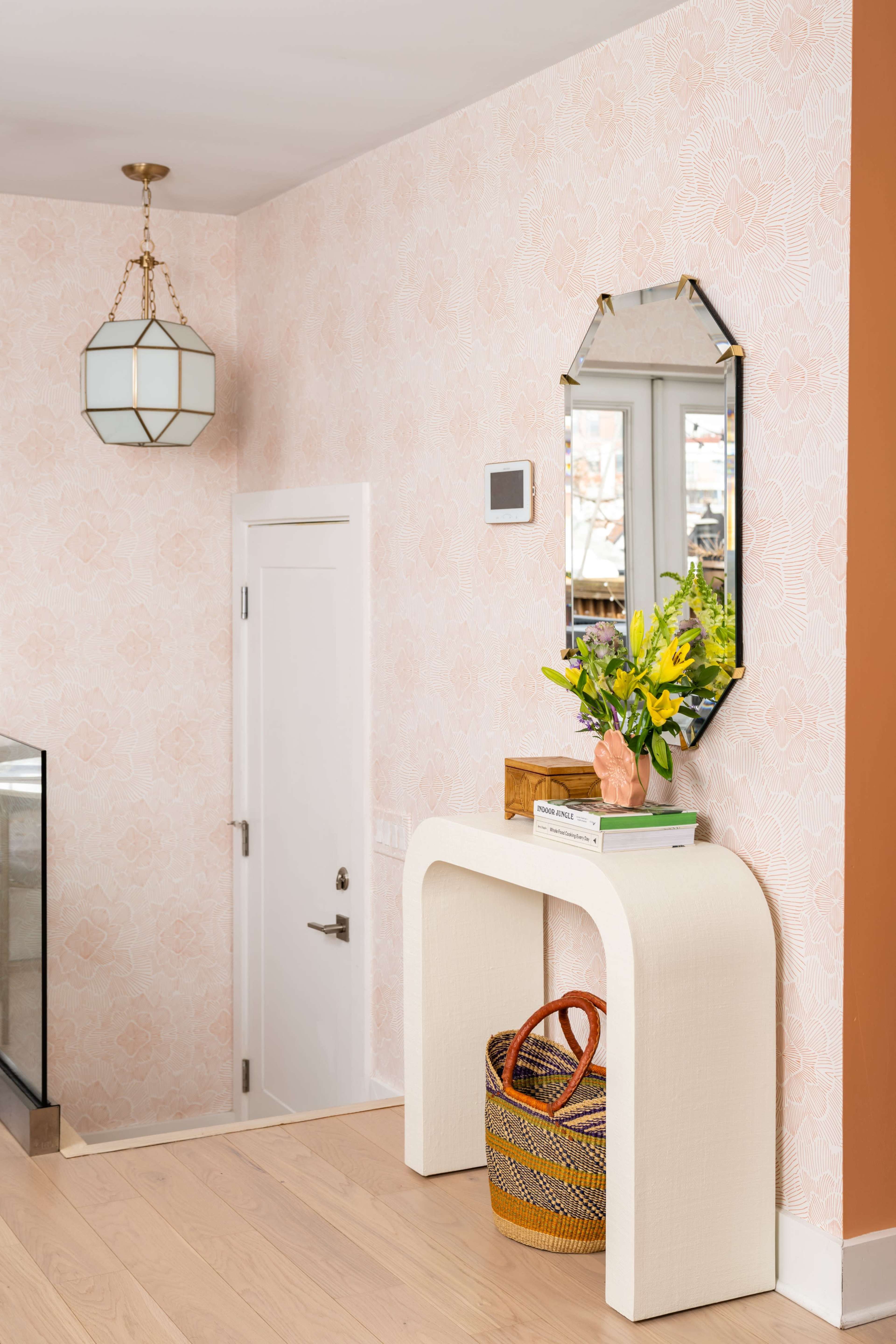 A pastel-colored hallway with a mirror and a floral arrangement on a console table next to a closed door.