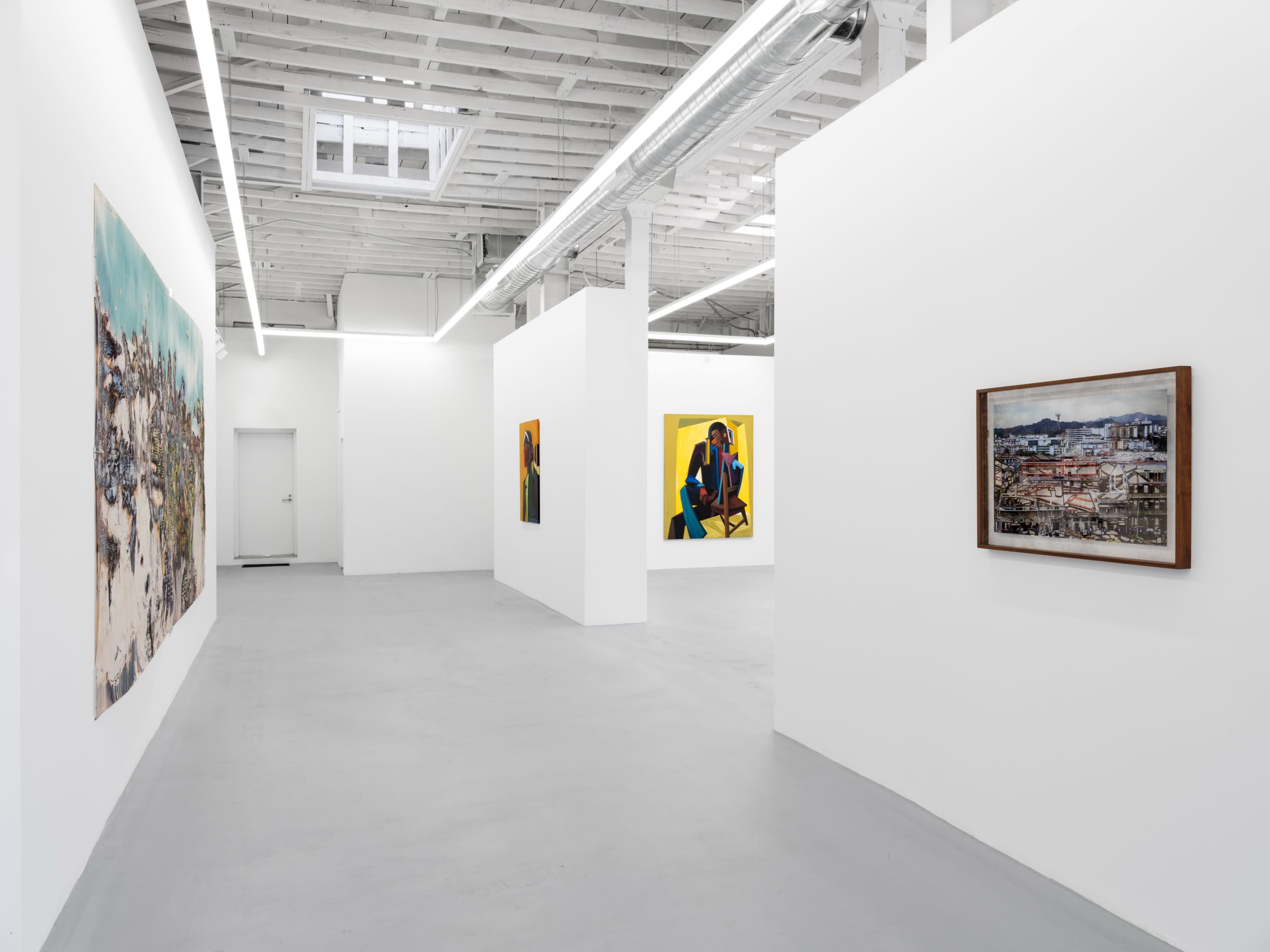 A modern art gallery with white walls, featuring several artworks displayed along the walls and a gray concrete floor.