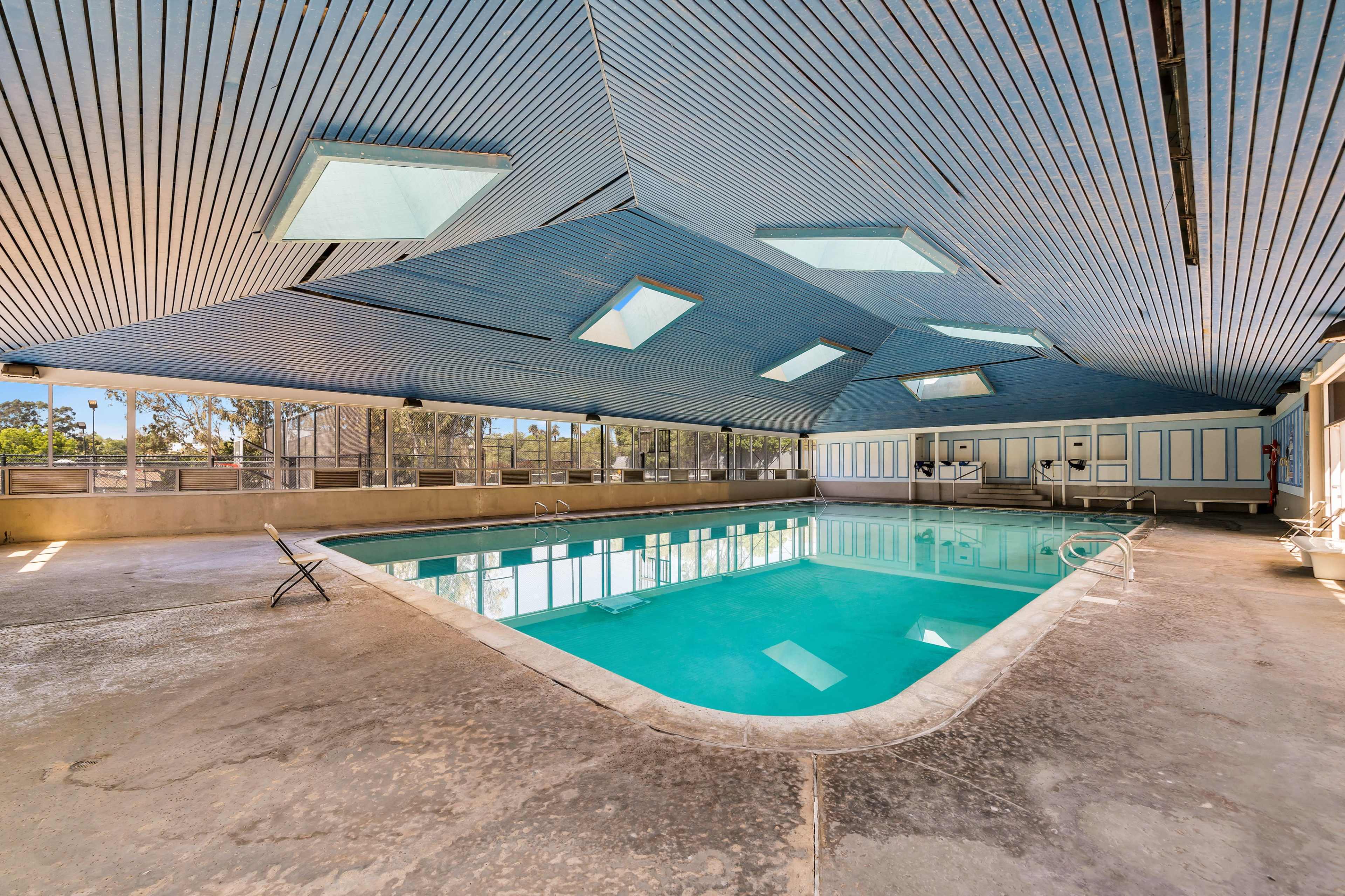 An indoor swimming pool with a unique angular ceiling design and large windows allowing natural light to enter.