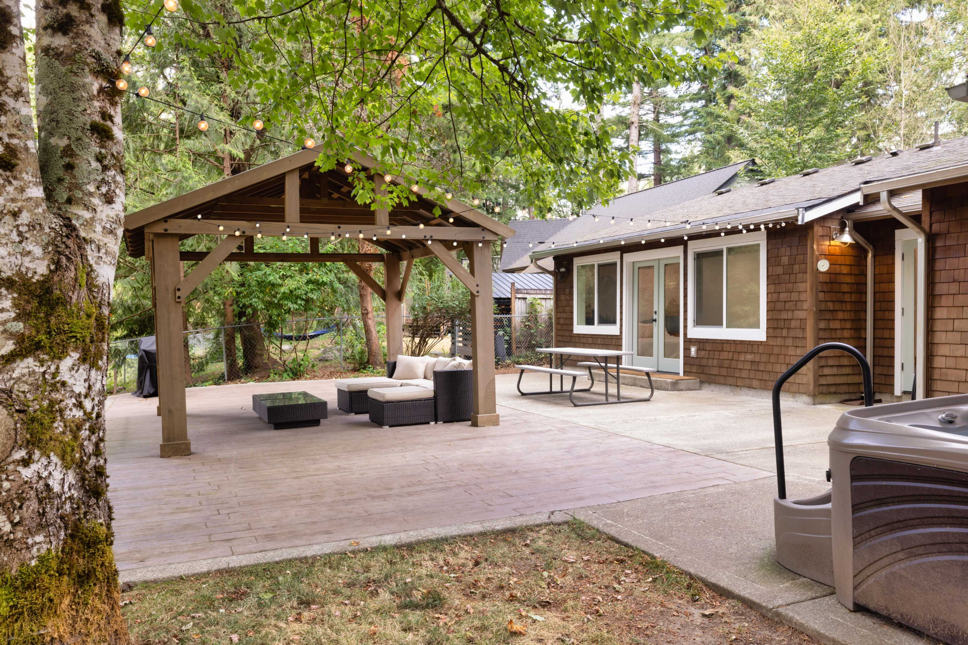 A backyard patio with a gazebo, outdoor seating area, and a hot tub, surrounded by trees.