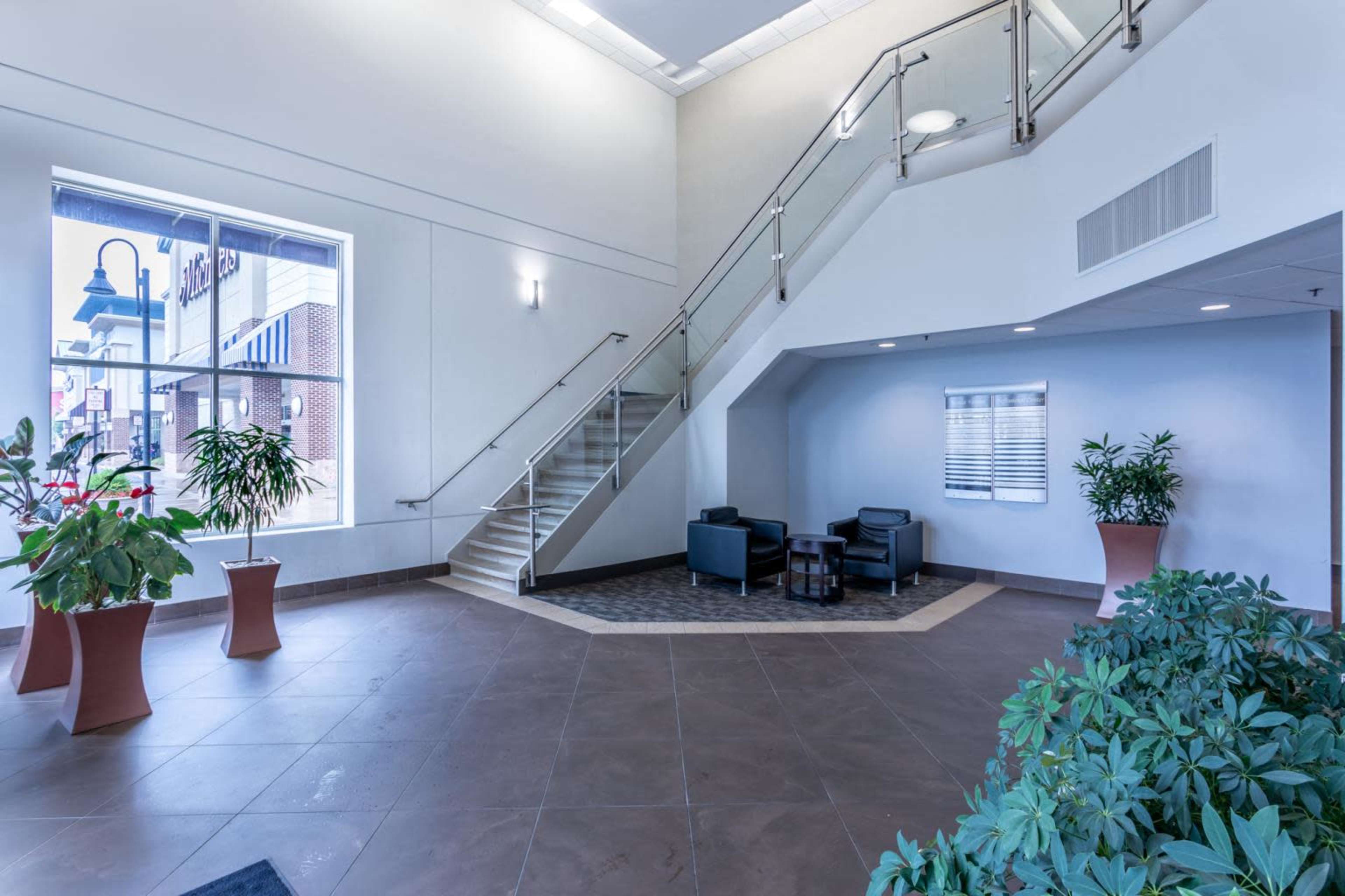 The image shows a spacious lobby area with a staircase, seating arrangement, and potted plants.