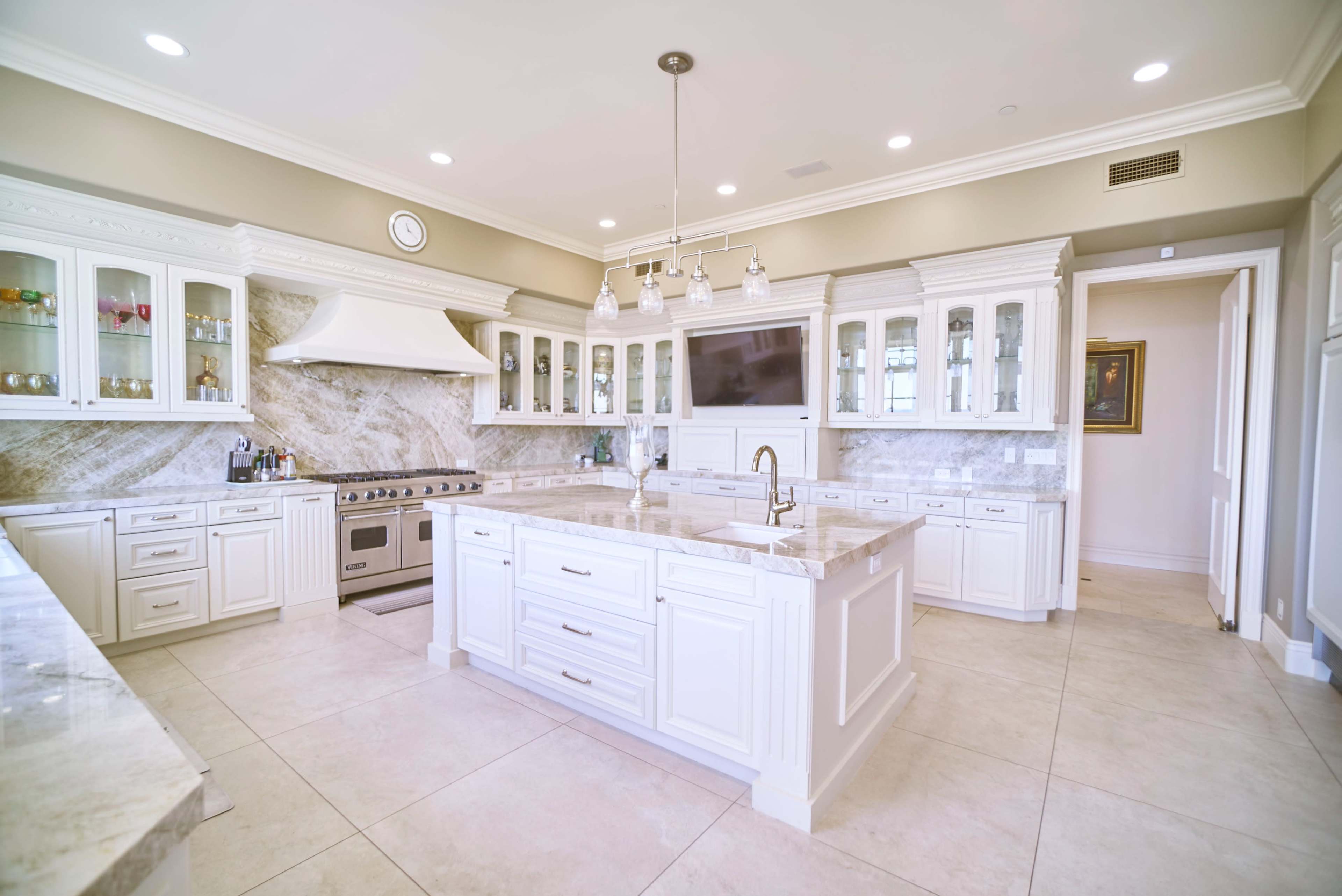 The image features a modern kitchen with white cabinetry, a large central island, stainless steel appliances, and marble countertops.