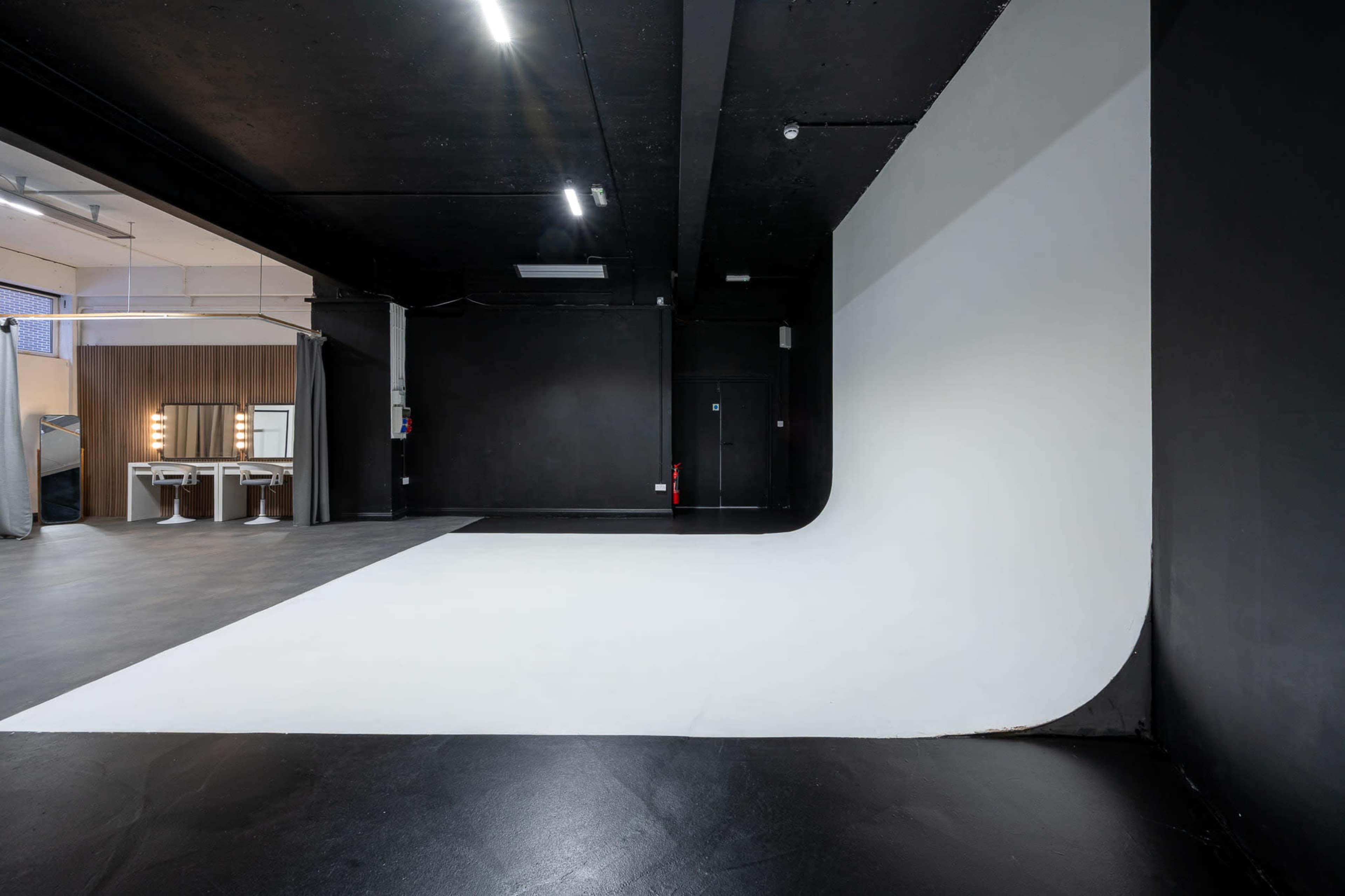 The image shows a photography studio featuring a white backdrop, black walls, and a seamless floor surface.