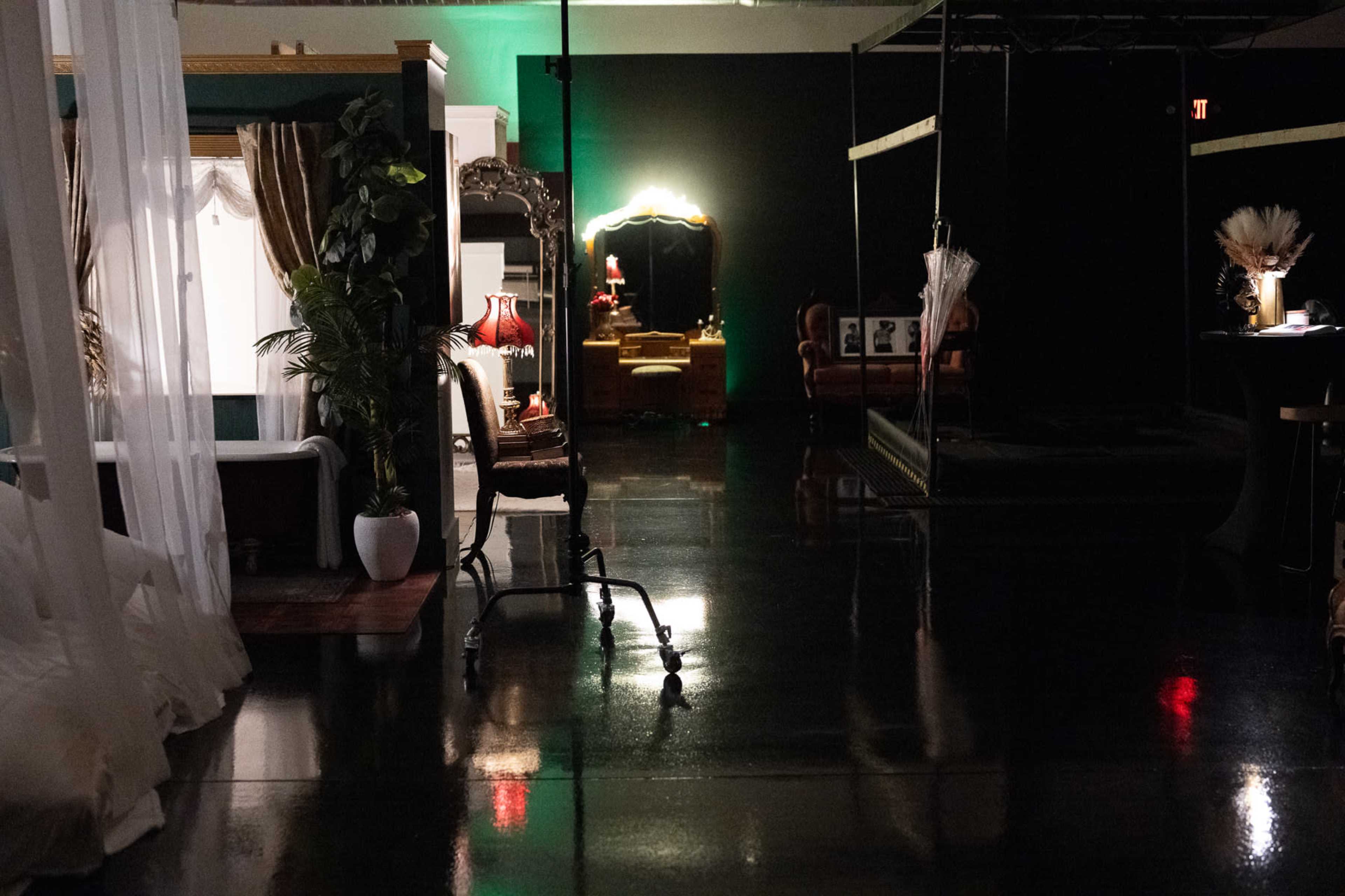 The image depicts a dimly lit interior space showcasing various furniture pieces, including a chair, a lamp, and a mirror, with reflective floors enhancing the ambiance.