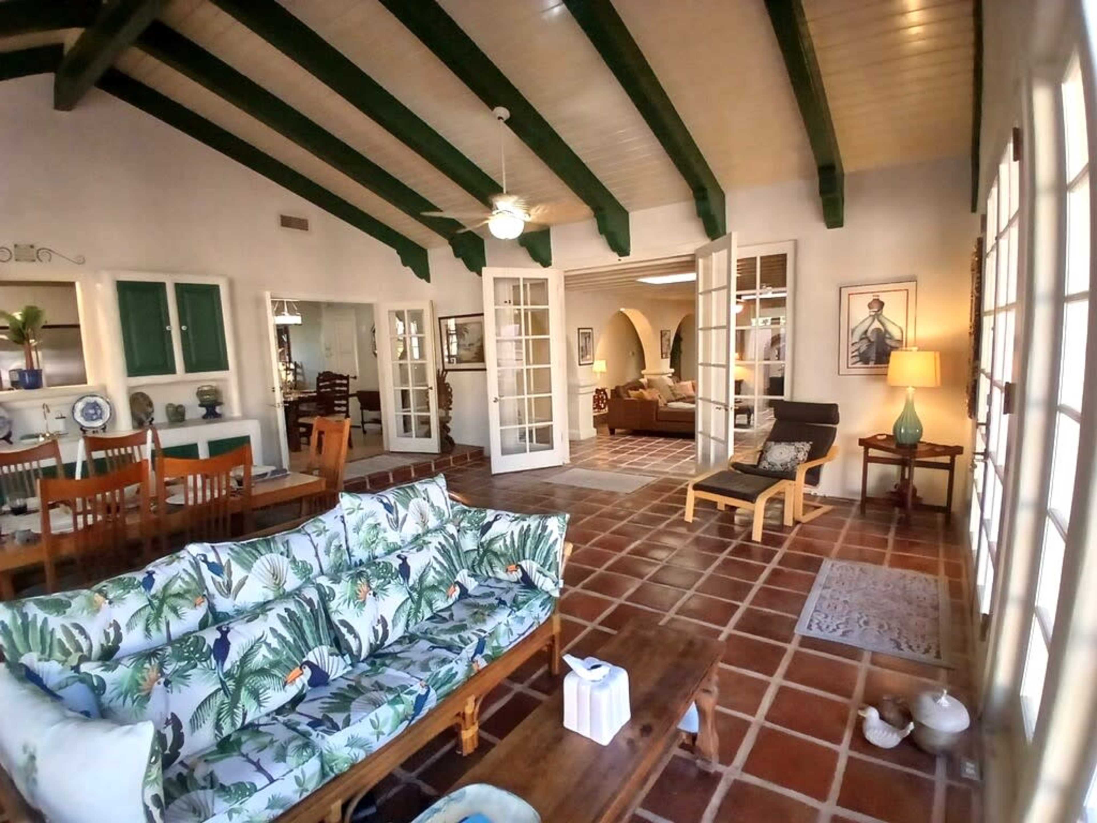 A spacious living area with a tropical-themed sofa, wooden furniture, and a view of adjoining rooms through French doors.