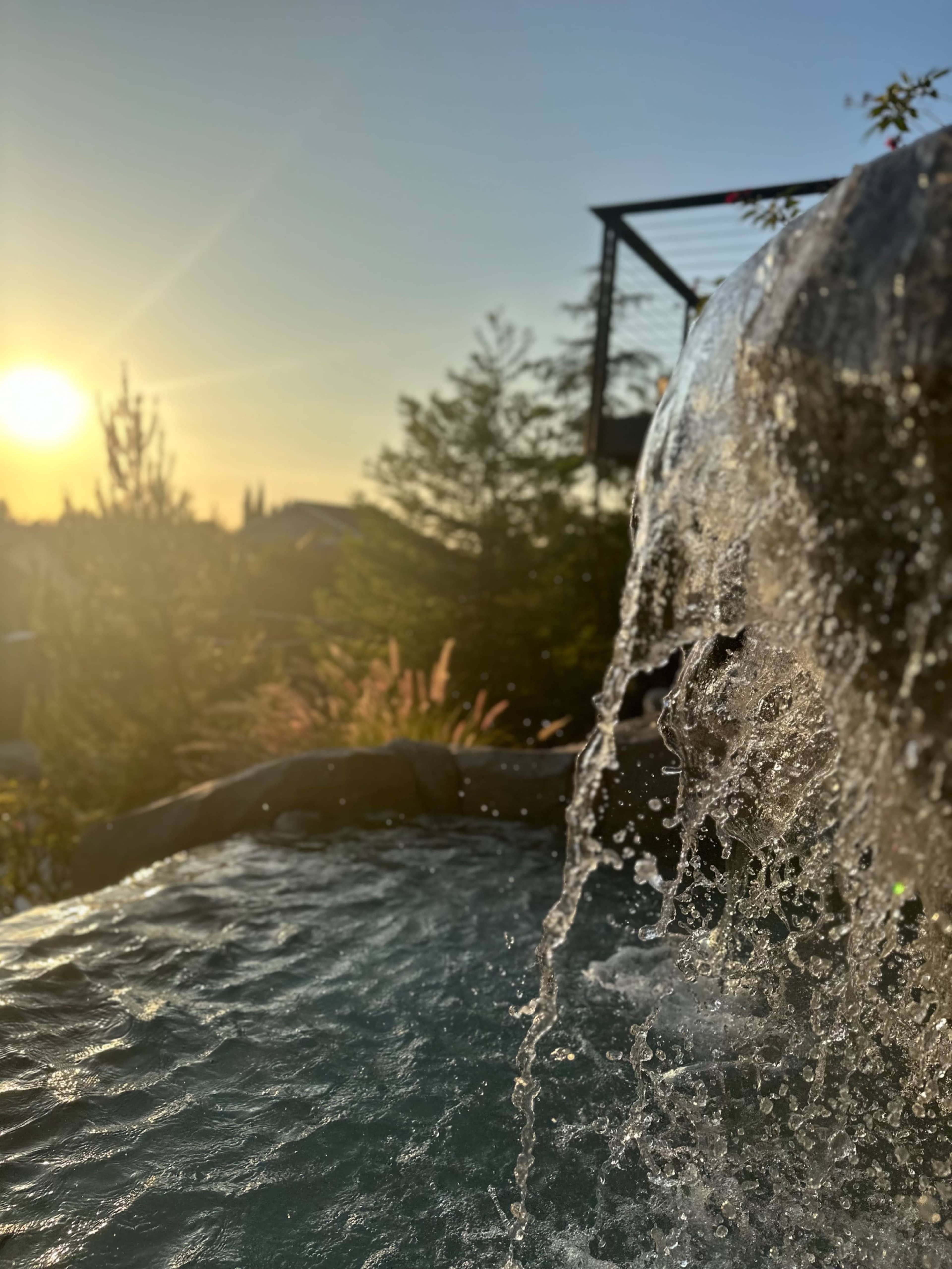 Water cascades over a rocky edge with the sunset casting light in the background.