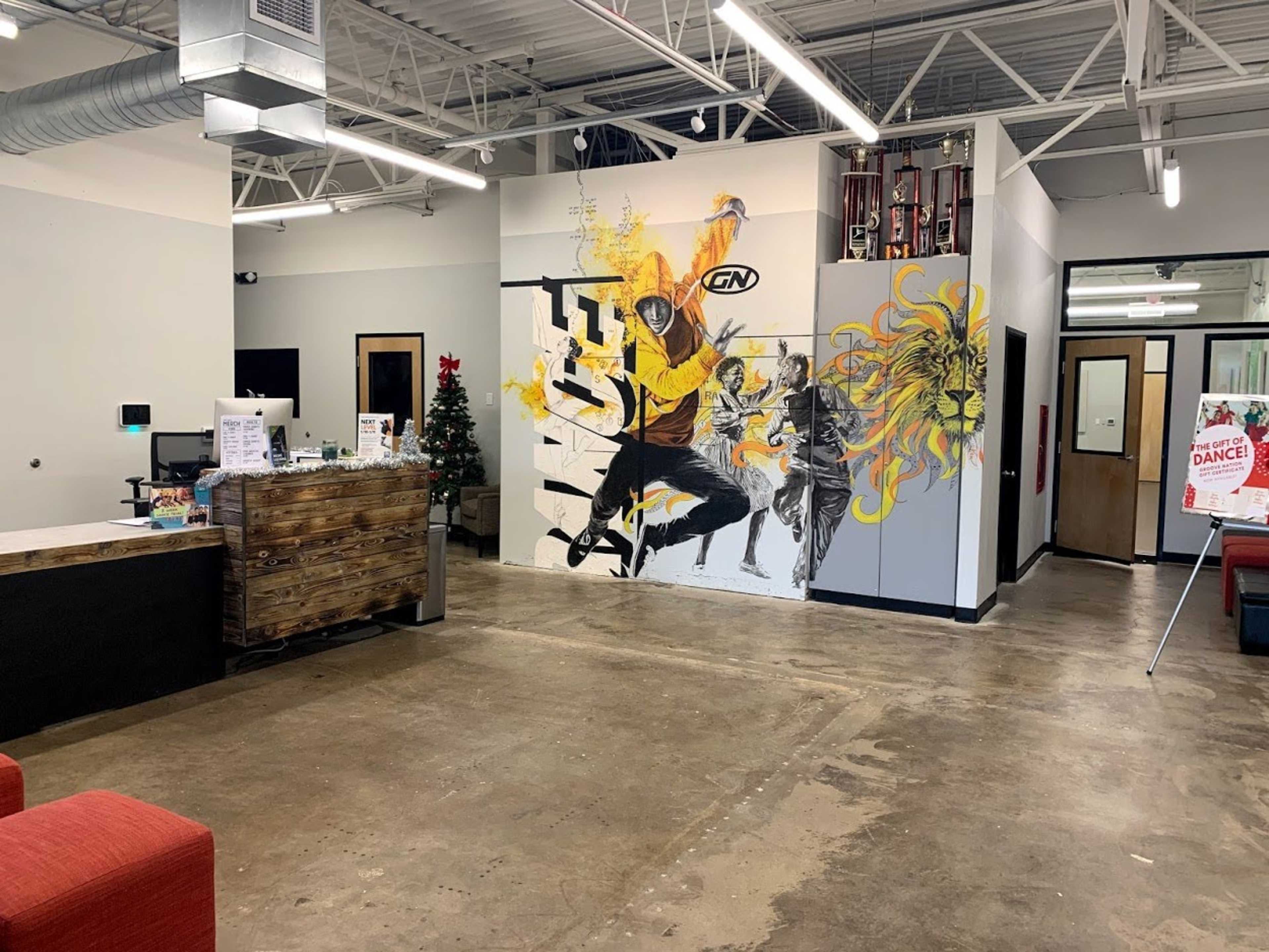 A spacious lobby area with a wooden reception desk, a mural depicting dancers on the wall, and a Christmas tree in the corner.