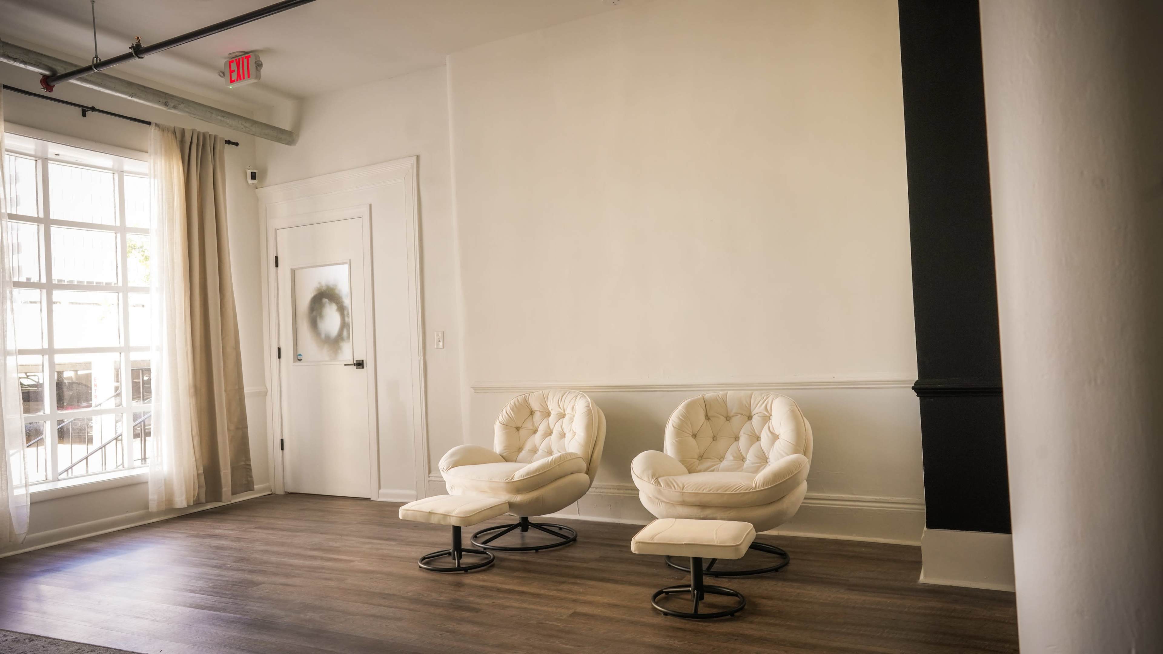 A bright room with two white, tufted chairs and a door with a frosted glass panel.