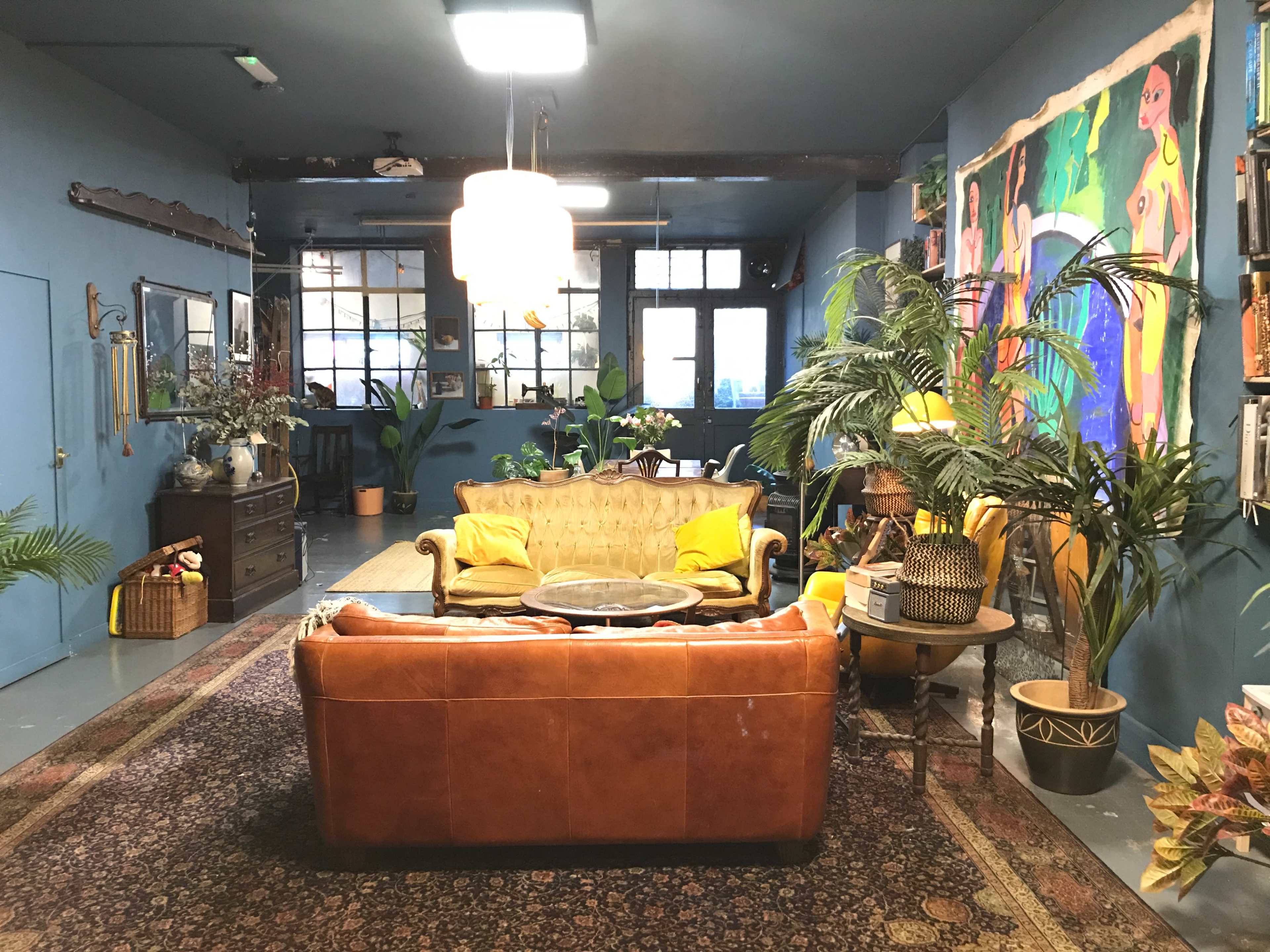 A spacious room decorated with blue walls, featuring a leather sofa, a round coffee table, plants, and colorful artwork.
