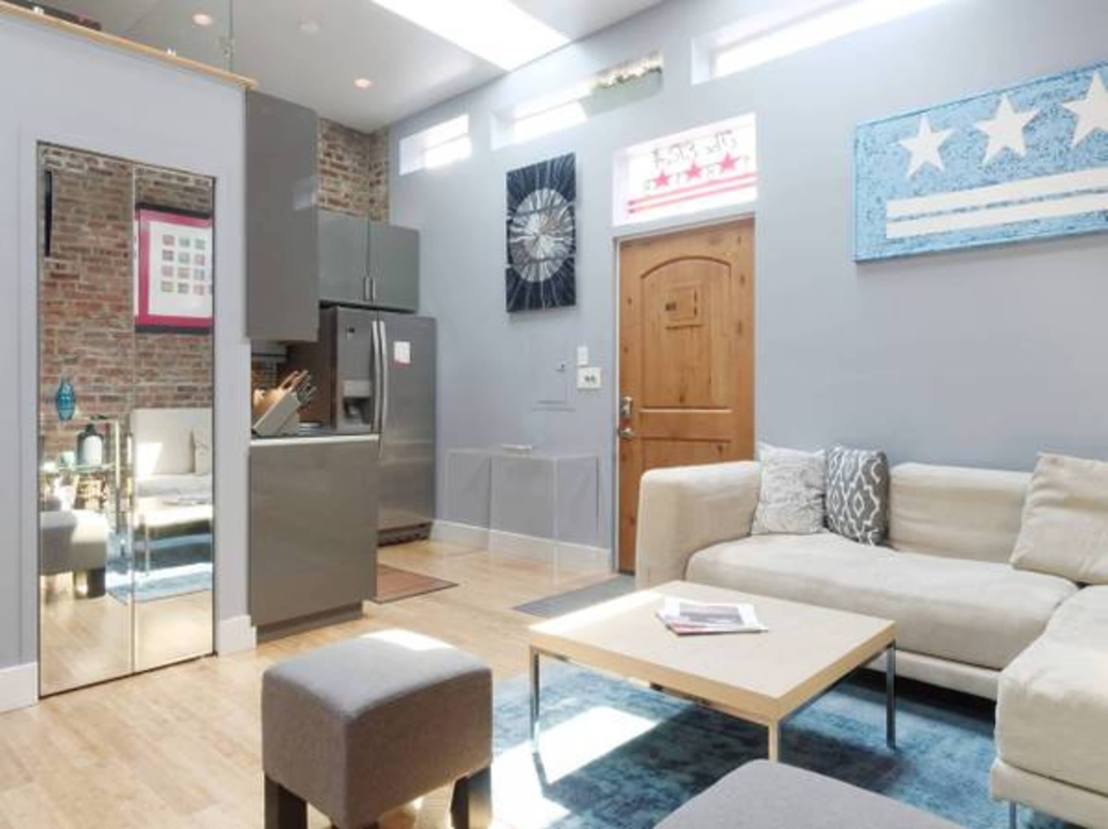 A modern living room with a sofa, coffee table, and a mirror, featuring exposed brick walls and a kitchen area in the background.