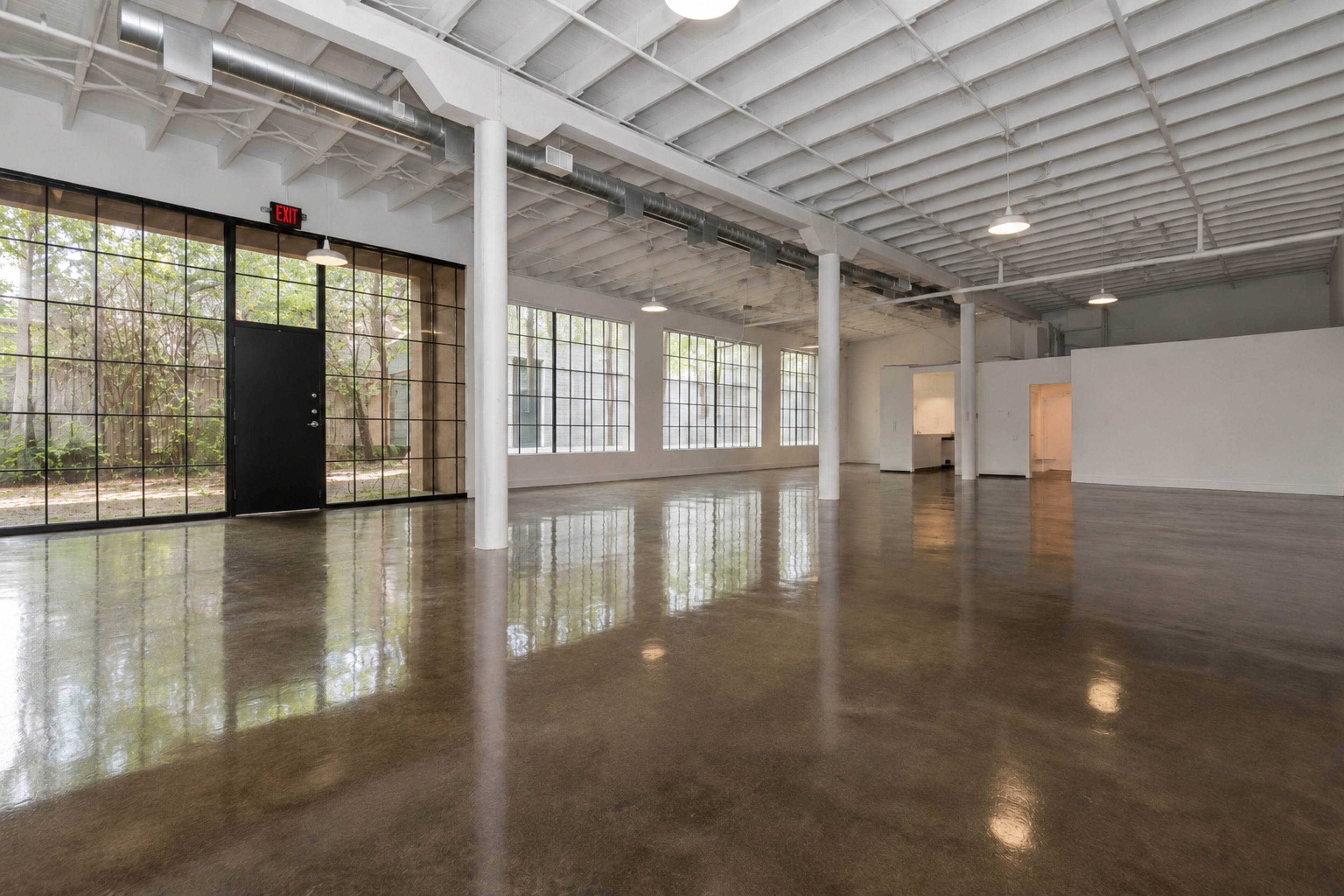 The image shows a spacious, minimalist interior with polished concrete floors, large windows, and white walls, creating an open and airy environment.