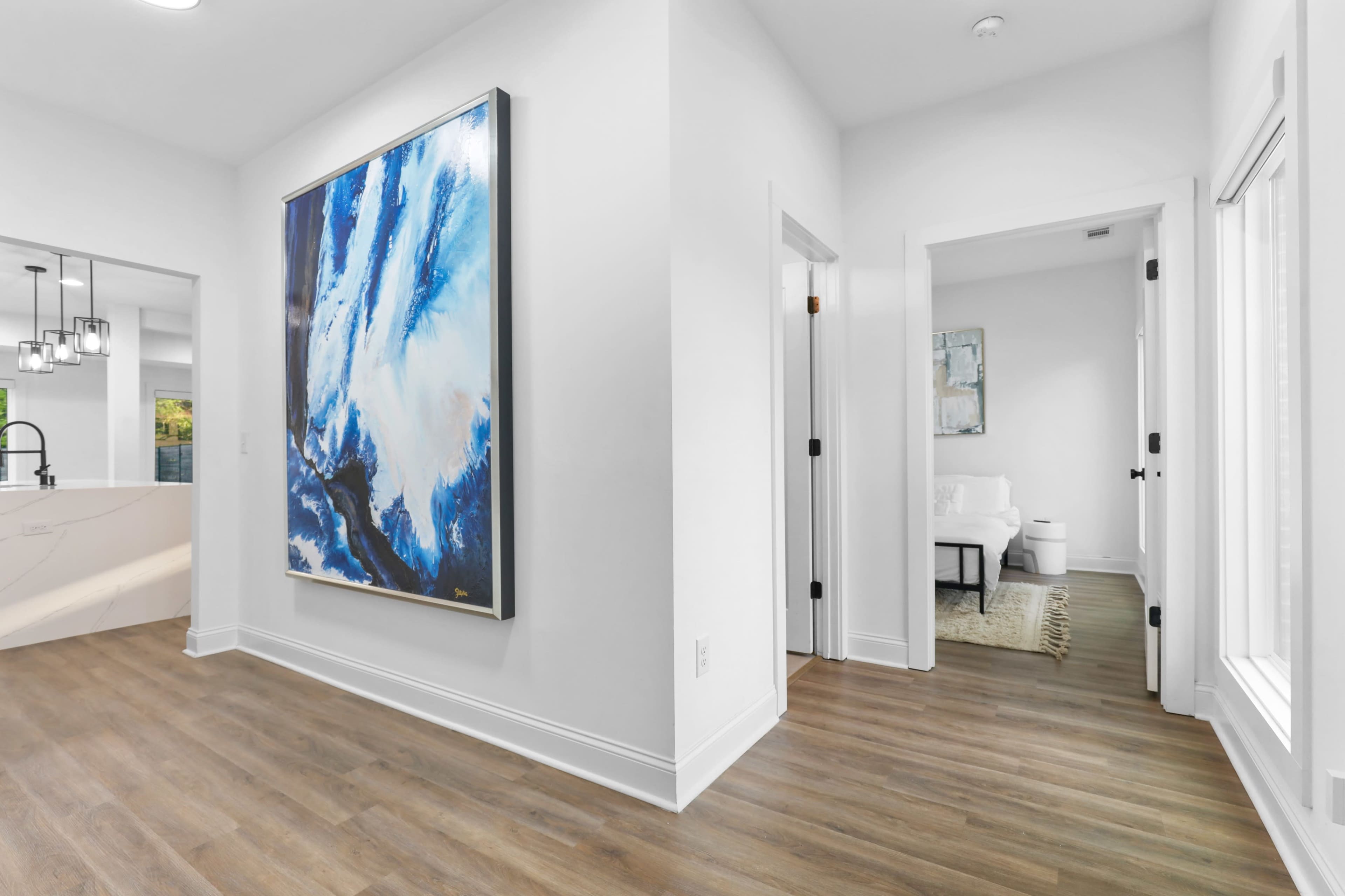 A modern entryway features a large abstract painting on a white wall, with wooden flooring and doors leading to adjacent rooms.
