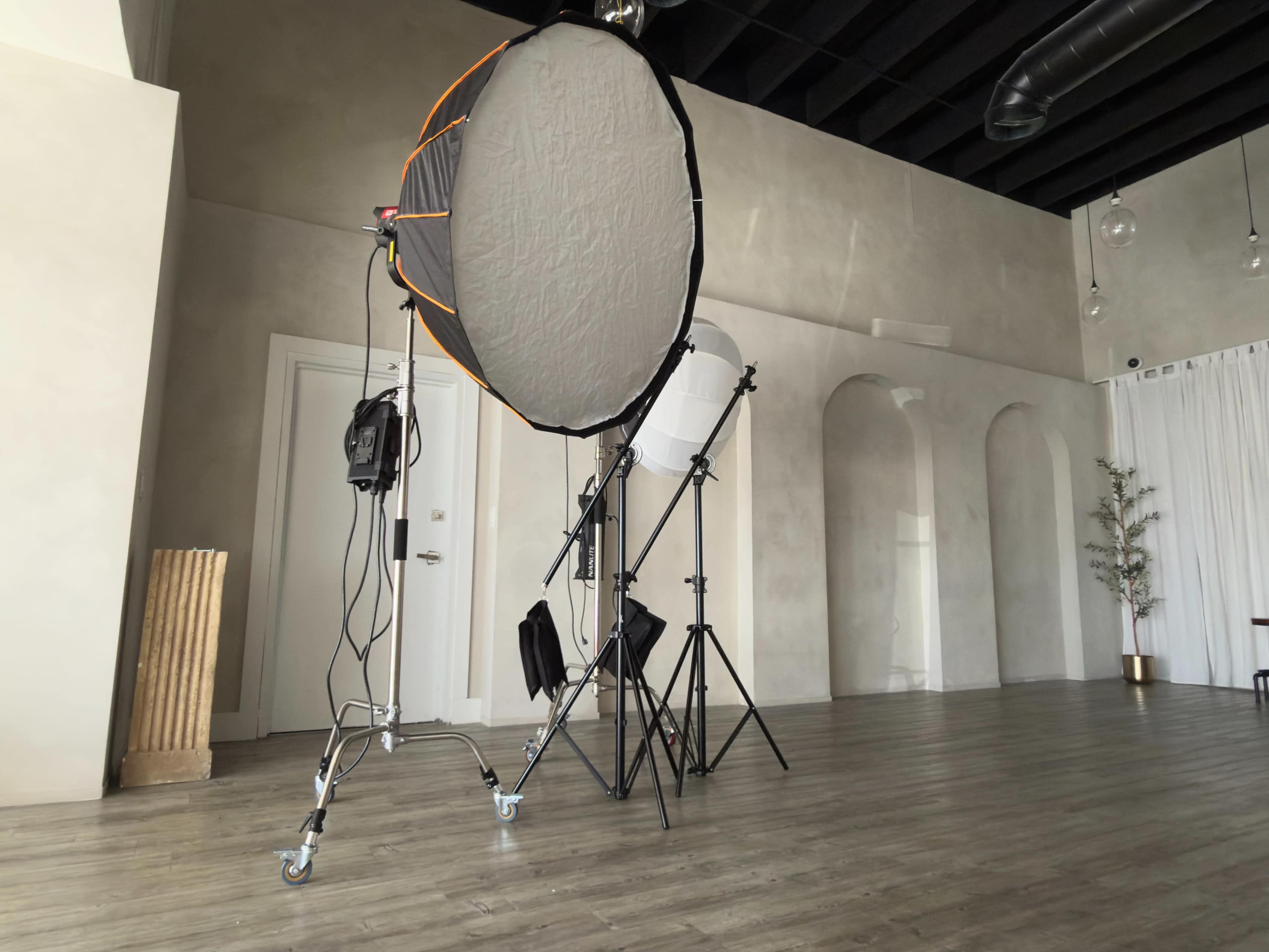 A large softbox and light stands are set up in a minimalist room with light-colored walls and a wooden floor.