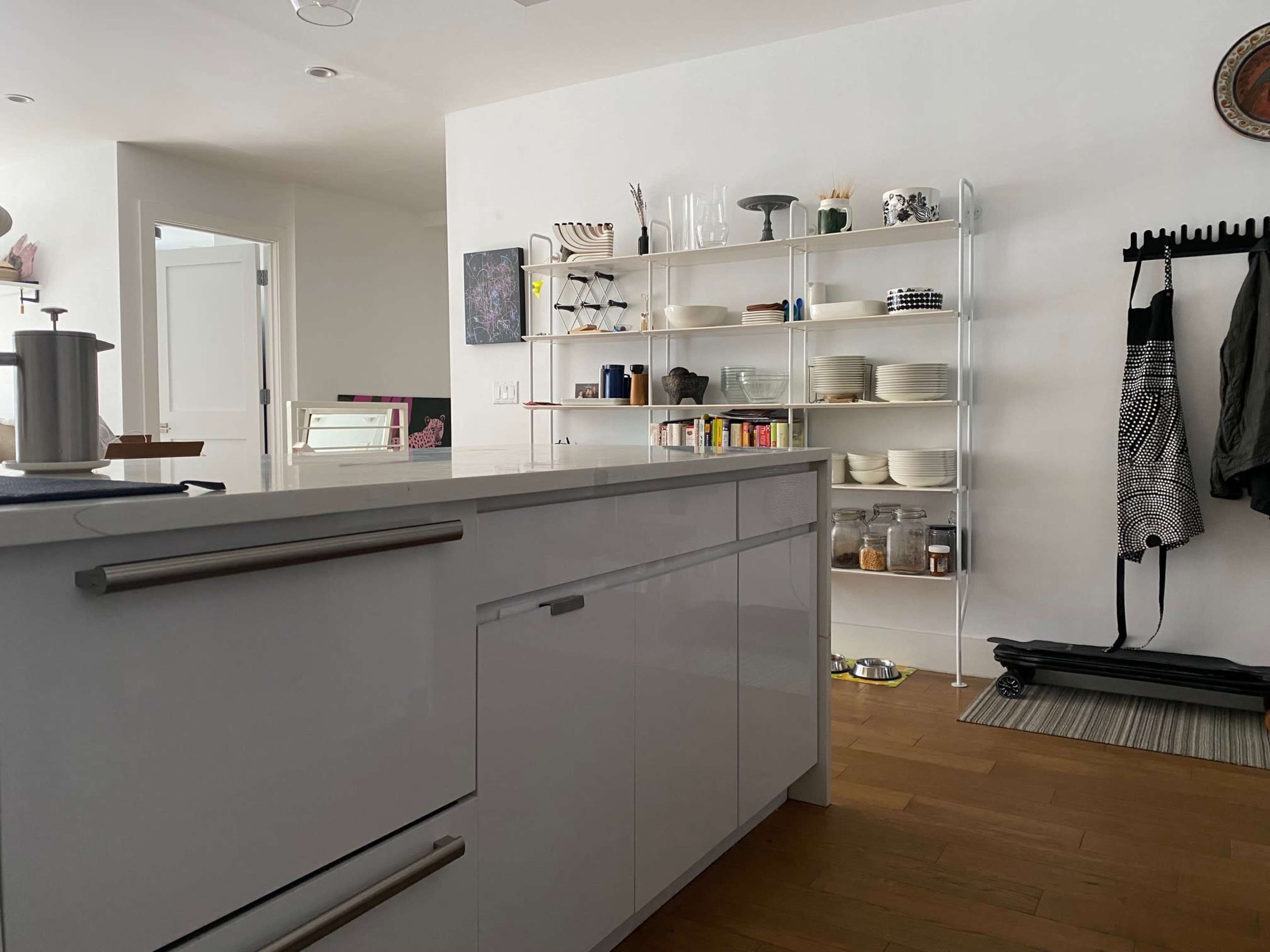 A modern kitchen features a white island, open shelving with dishes and jars, and a doorway leading to another room.