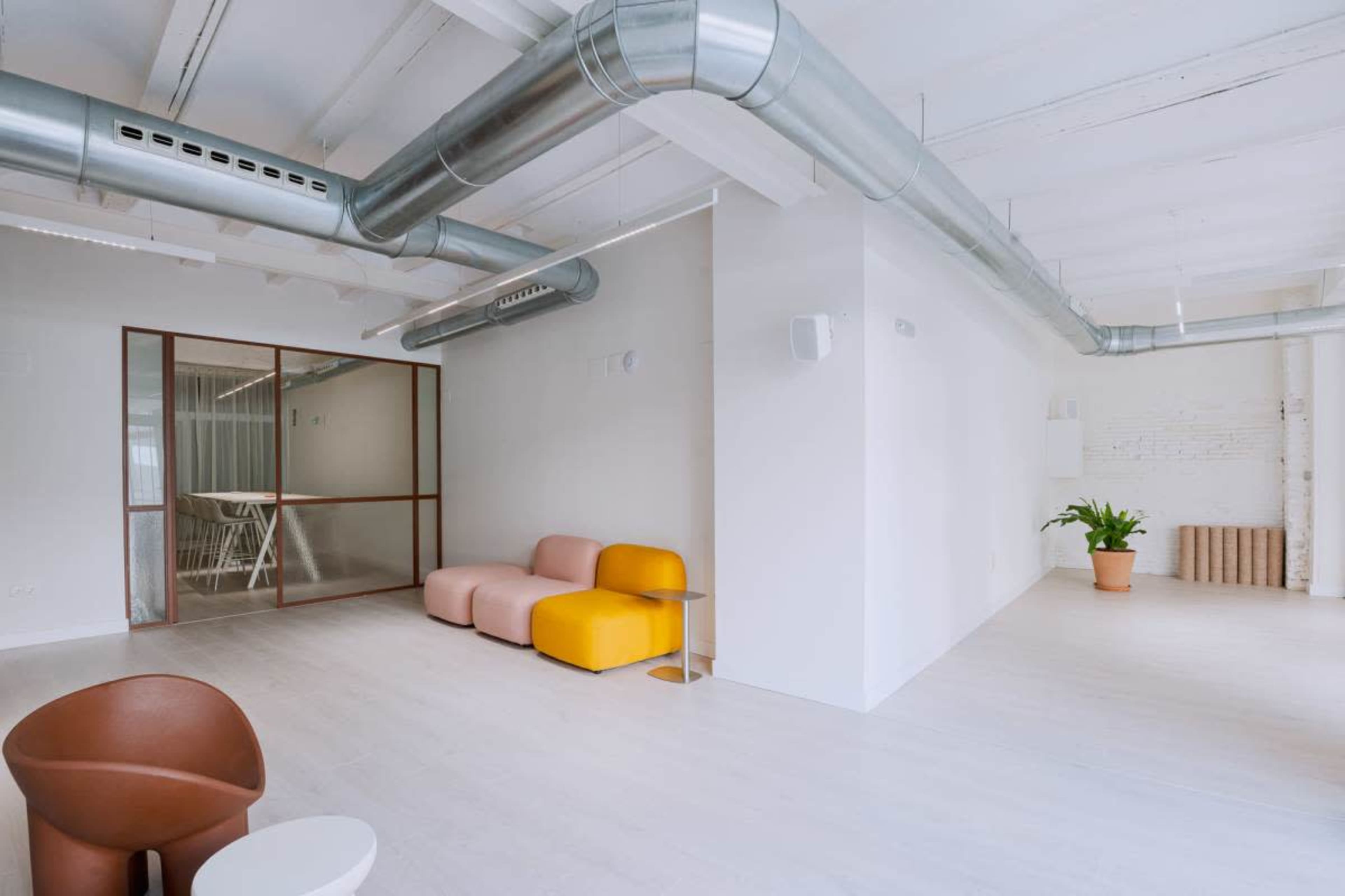 The image shows a spacious, modern office interior with exposed ductwork and a seating area featuring pastel-colored couches.