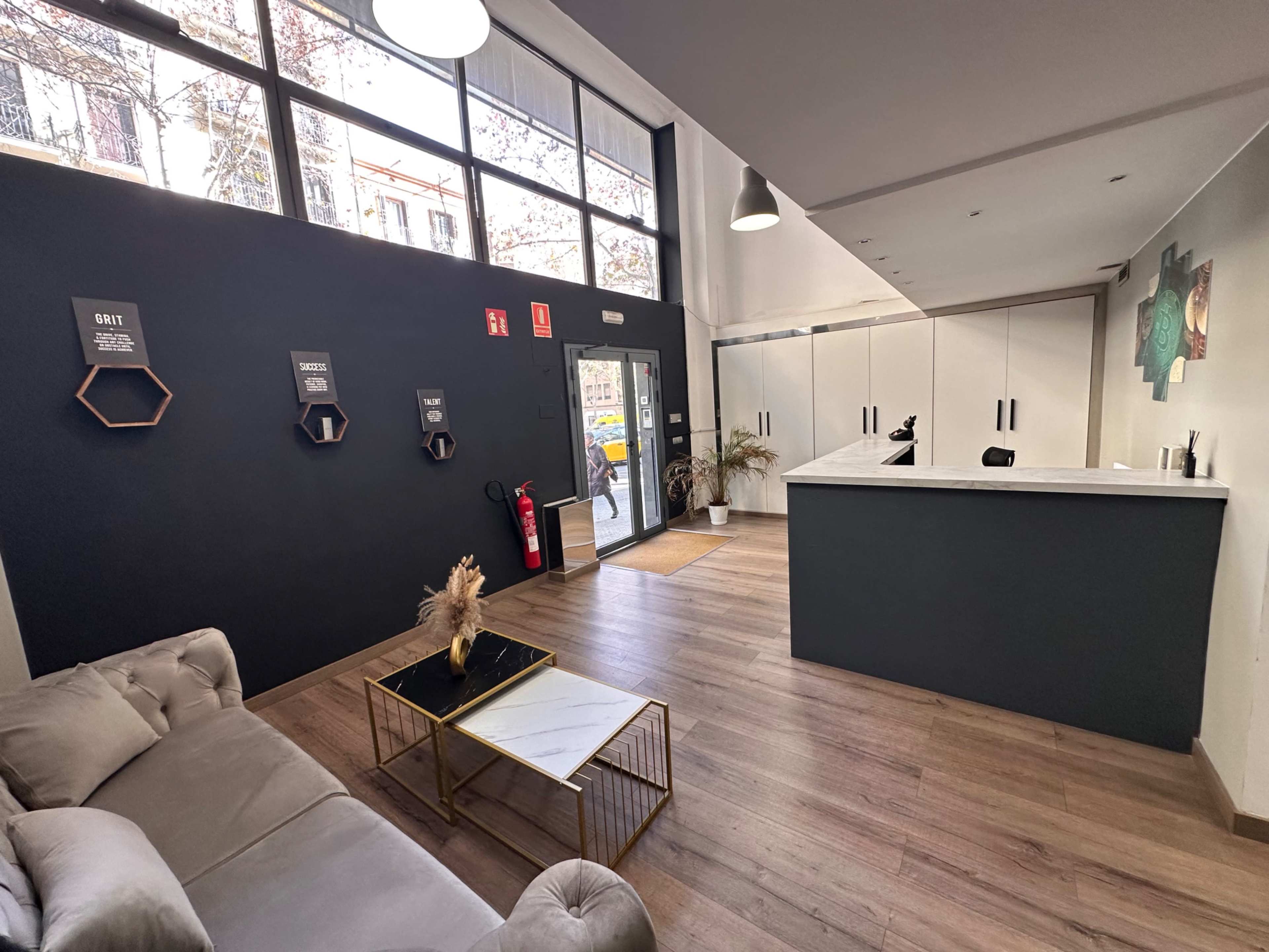 The image shows a modern reception area with a desk, seating, and dark walls adorned with decor and wall-mounted shelves.