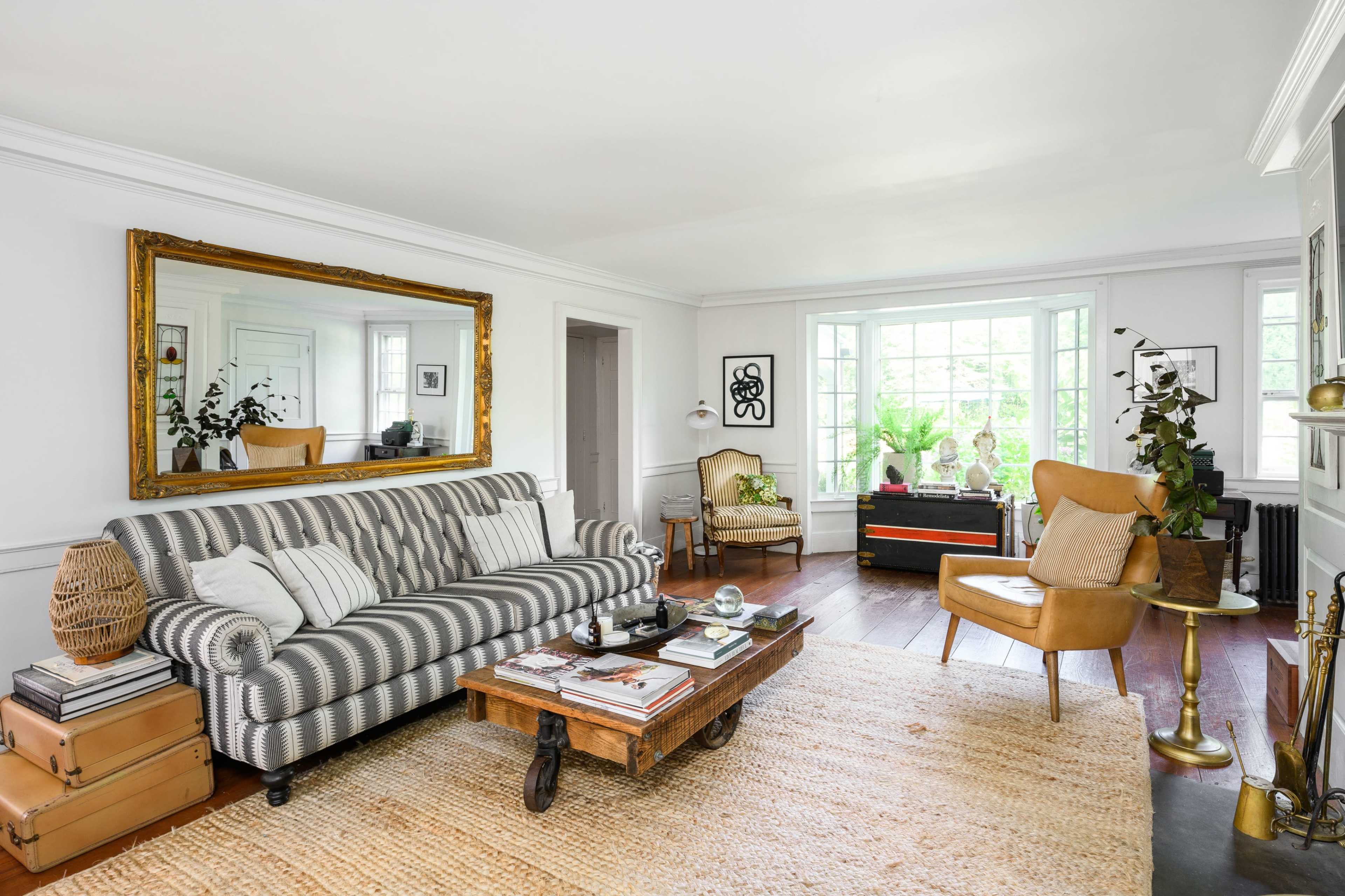 The living room features a striped sofa, a wooden coffee table, and large windows allowing natural light.