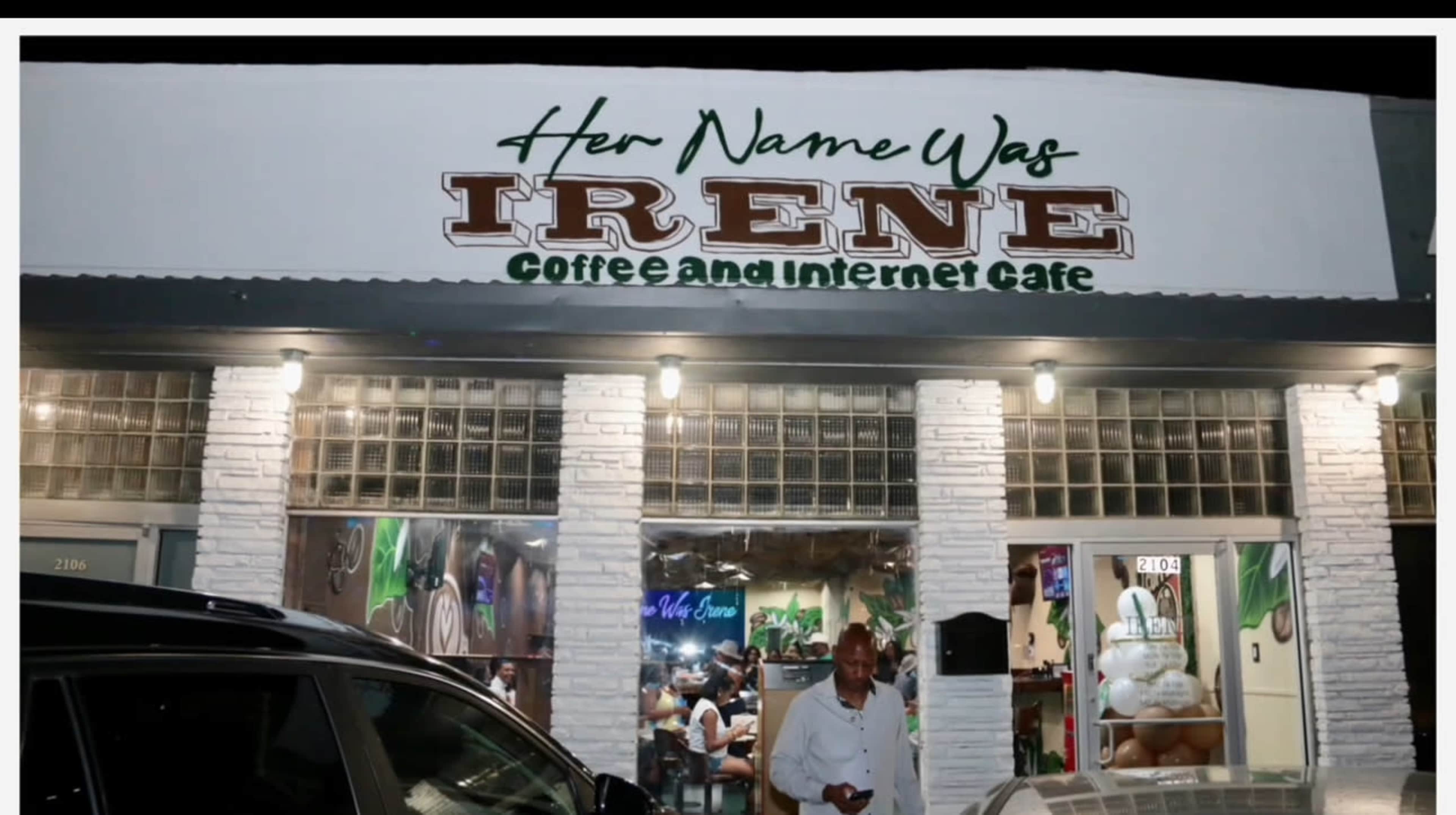 The image shows a coffee and internet café named "Her Name Was IRENE," with a lit sign and an entrance where a man stands outside.