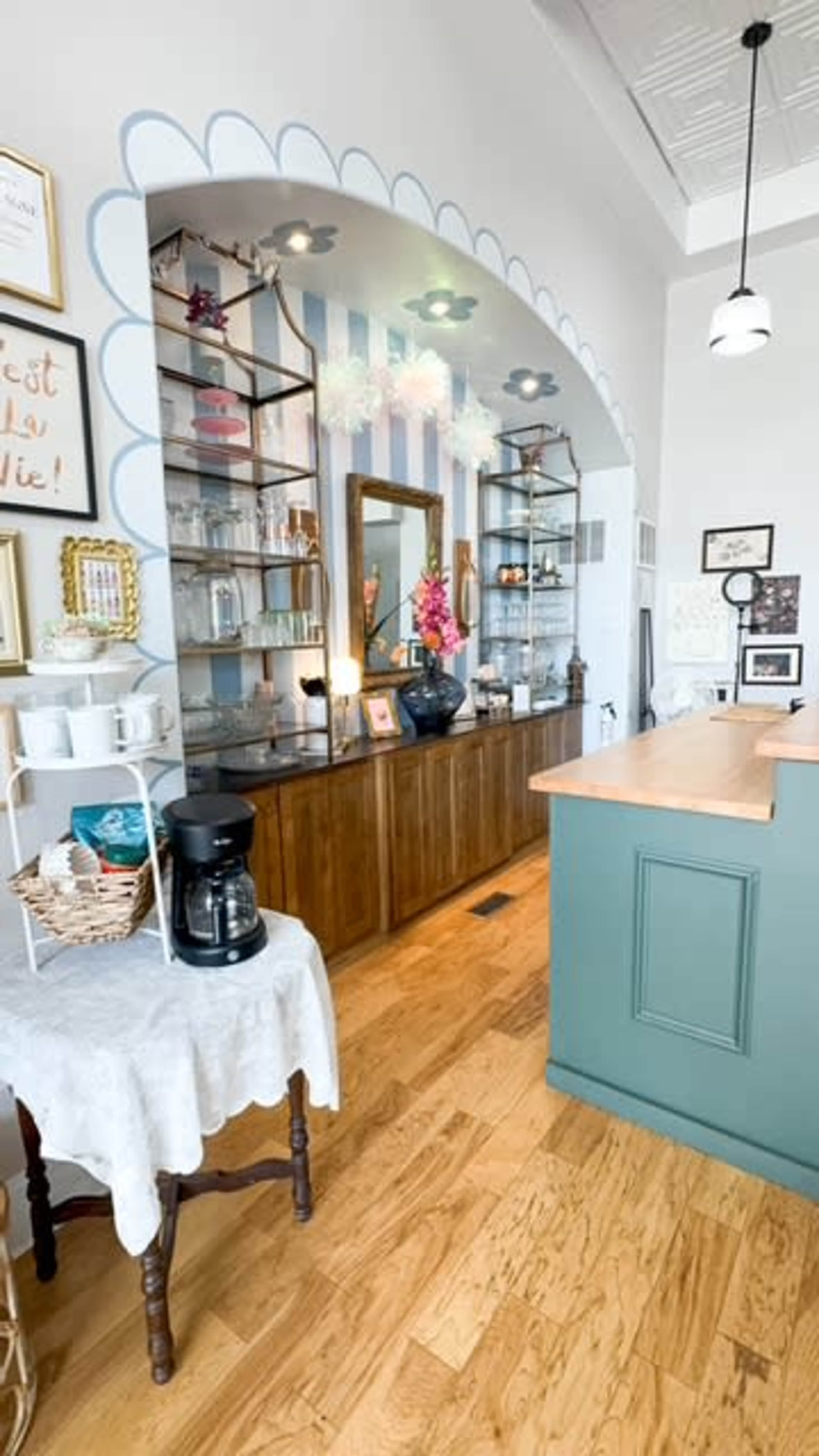 The image shows a cozy café interior featuring a wooden counter, shelves with decorative items, and a coffee maker on a small table.