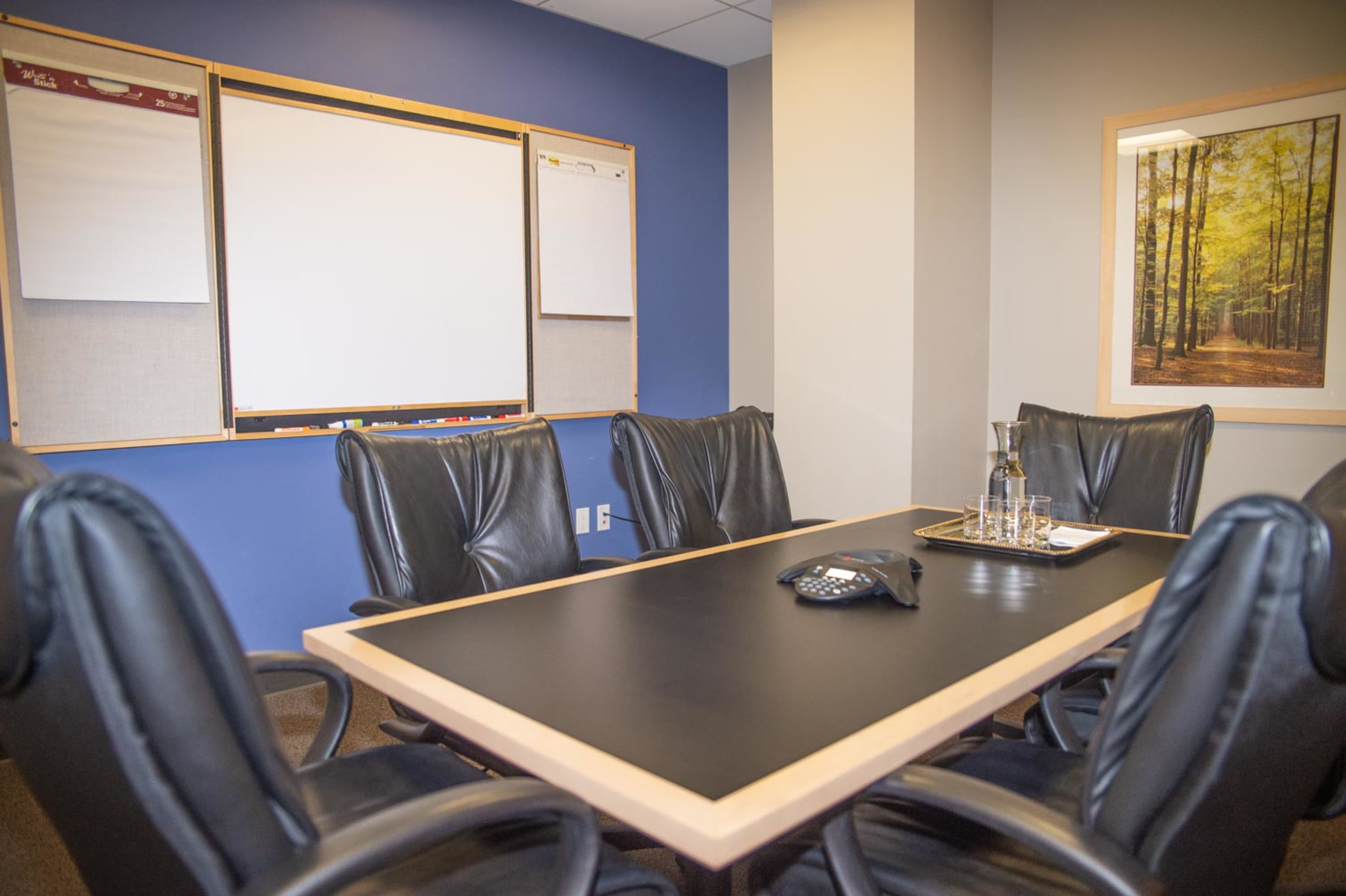 A conference room features a large table surrounded by black leather chairs, with a whiteboard and flip charts on the wall.