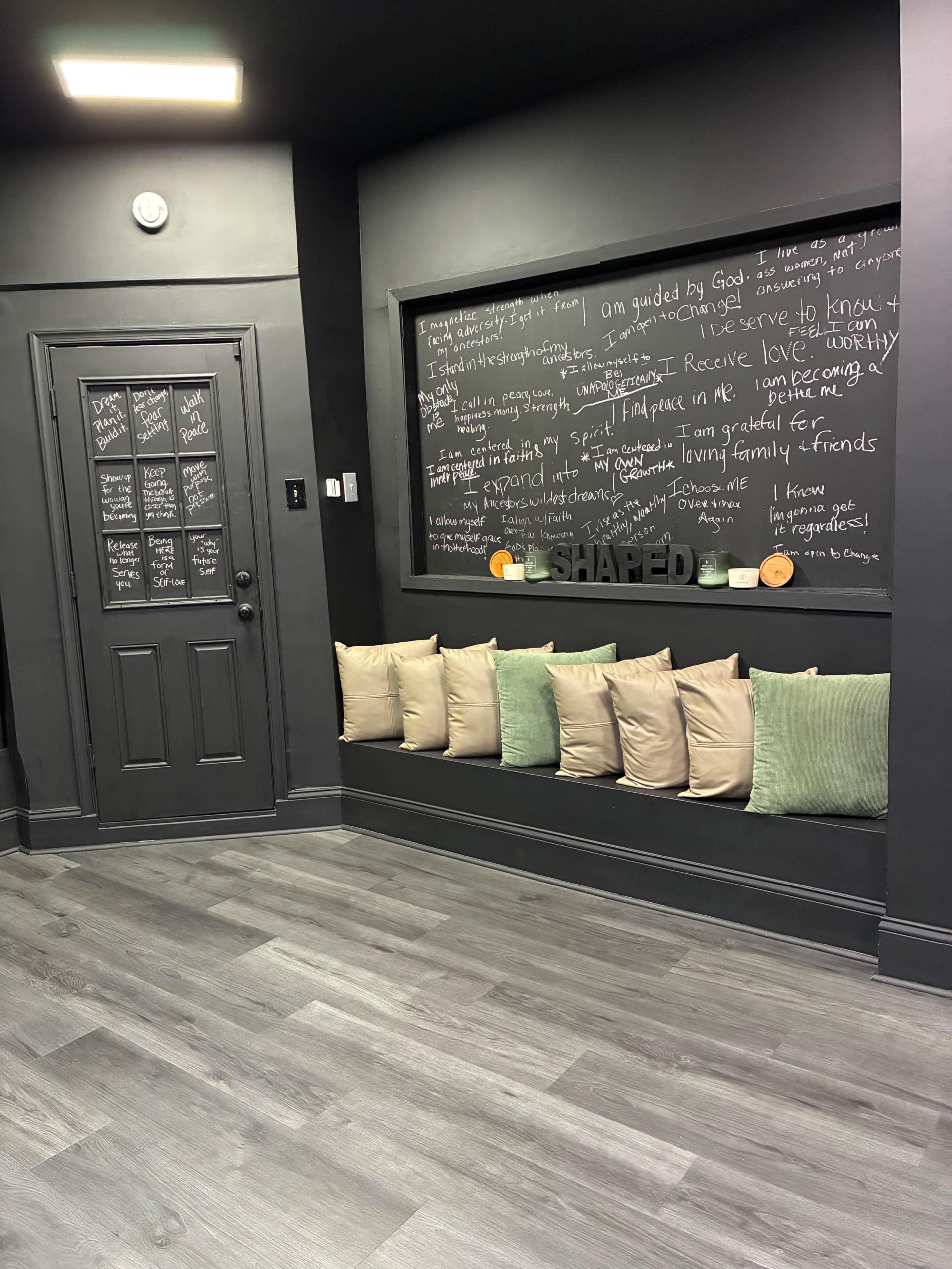 The interior features a dark-painted wall with a chalkboard filled with handwritten notes and a seating area lined with beige cushions.