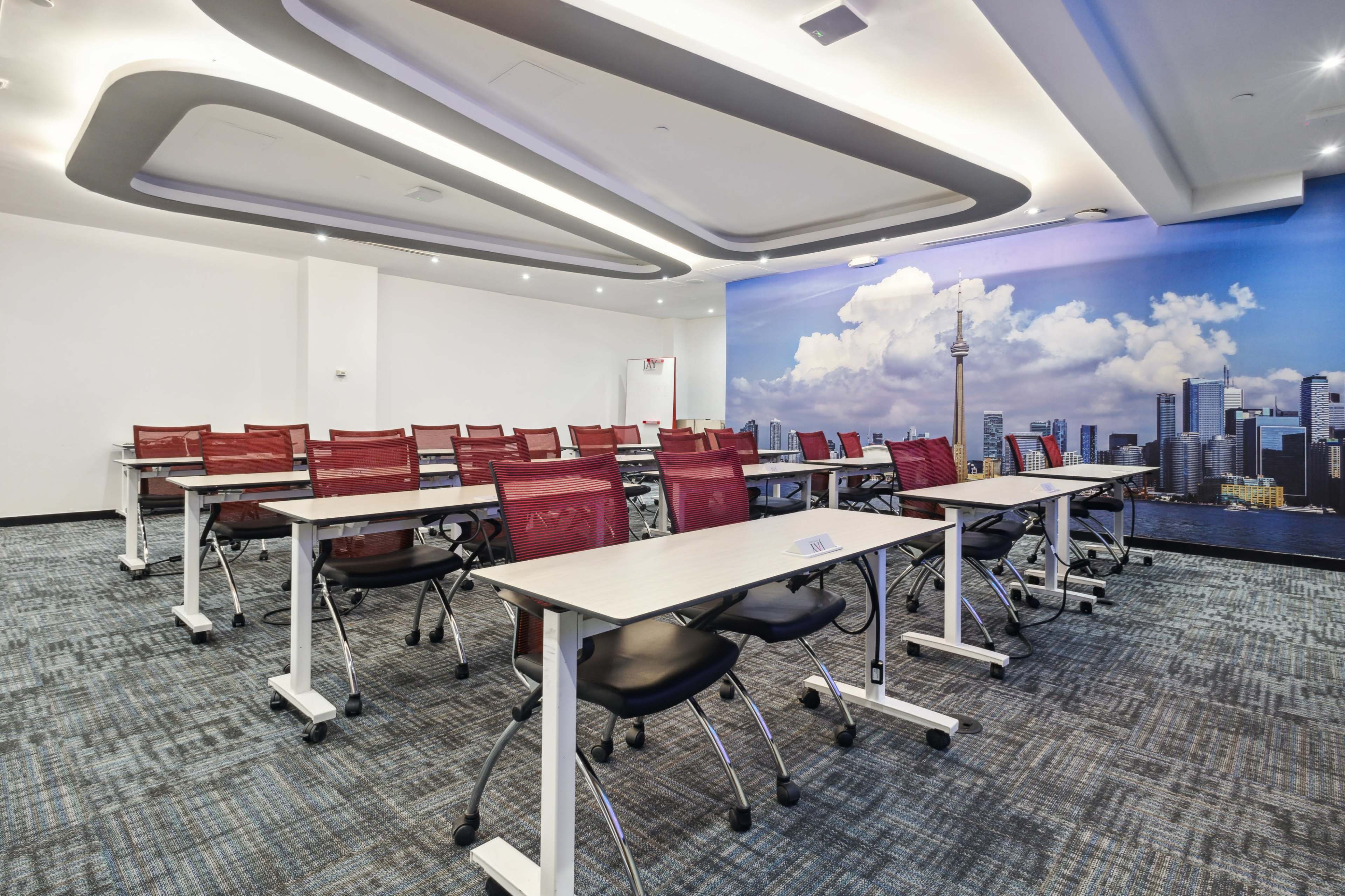 A modern conference room features rows of tables and chairs, with a large mural of a city skyline on one wall.