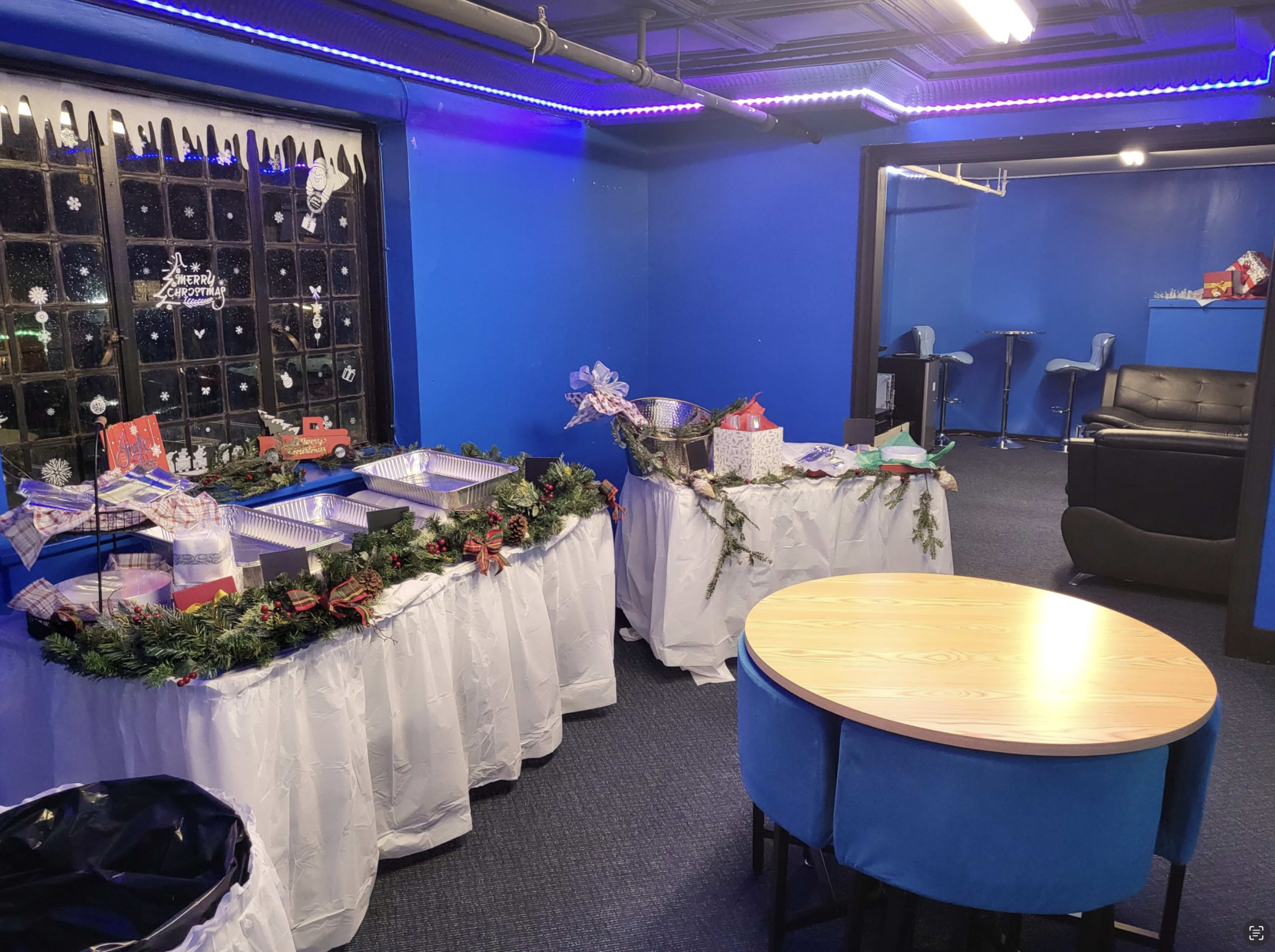 A blue-themed room features tables with festive decorations, a seating area, and a bar in the background.