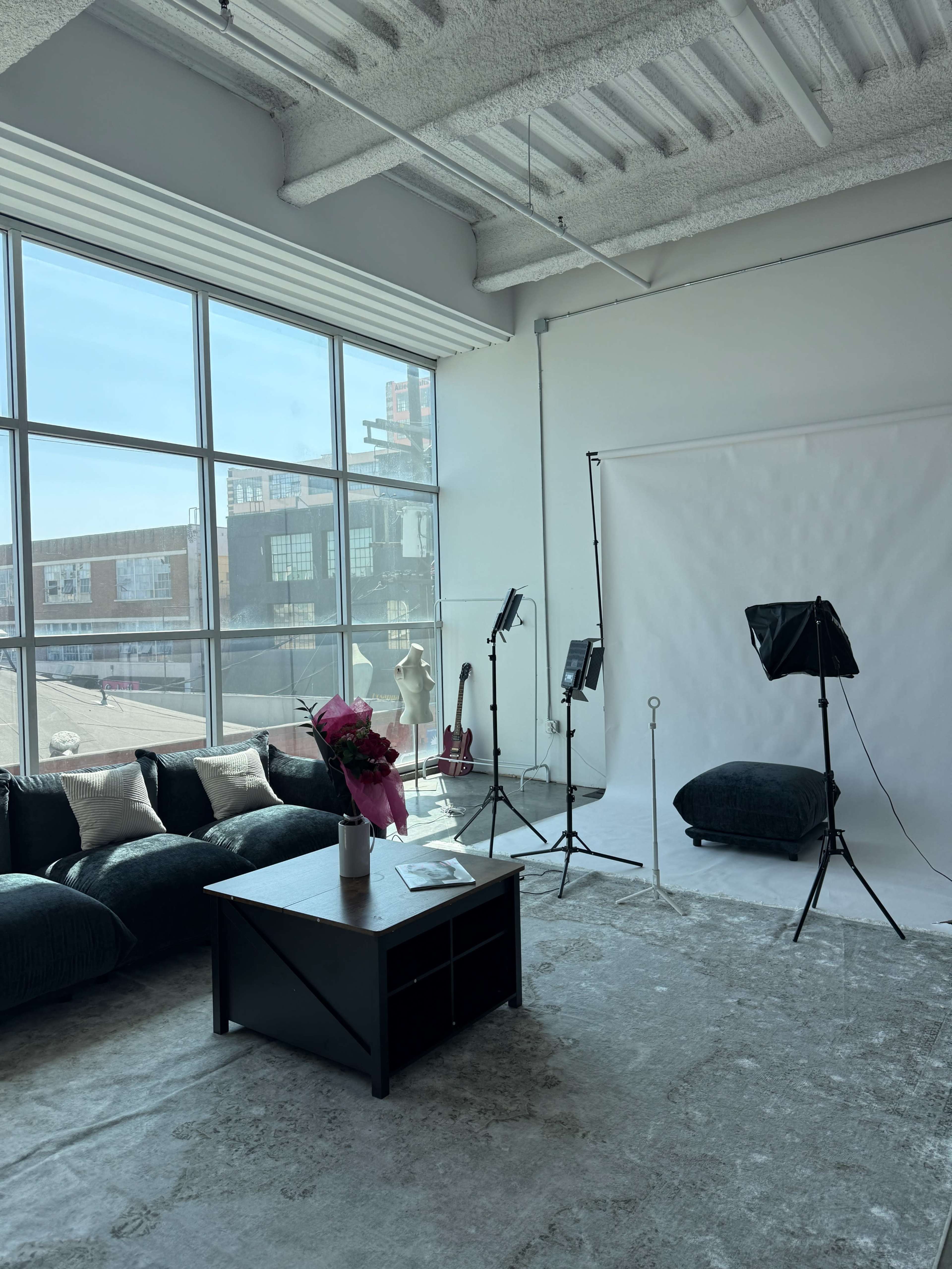 The image shows a well-lit studio space featuring a sofa, a coffee table, and a backdrop with lighting equipment set up for photography.