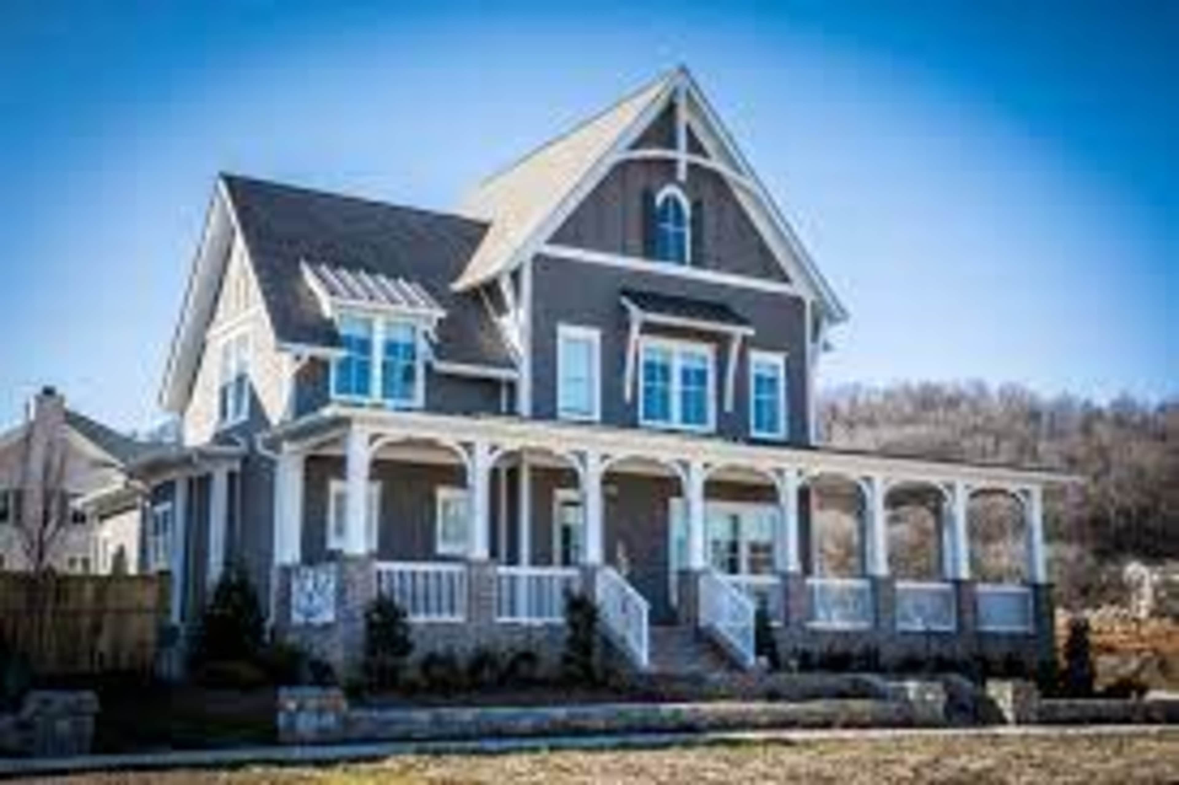 A large, gray two-story house features a prominent front porch and a gable roof.