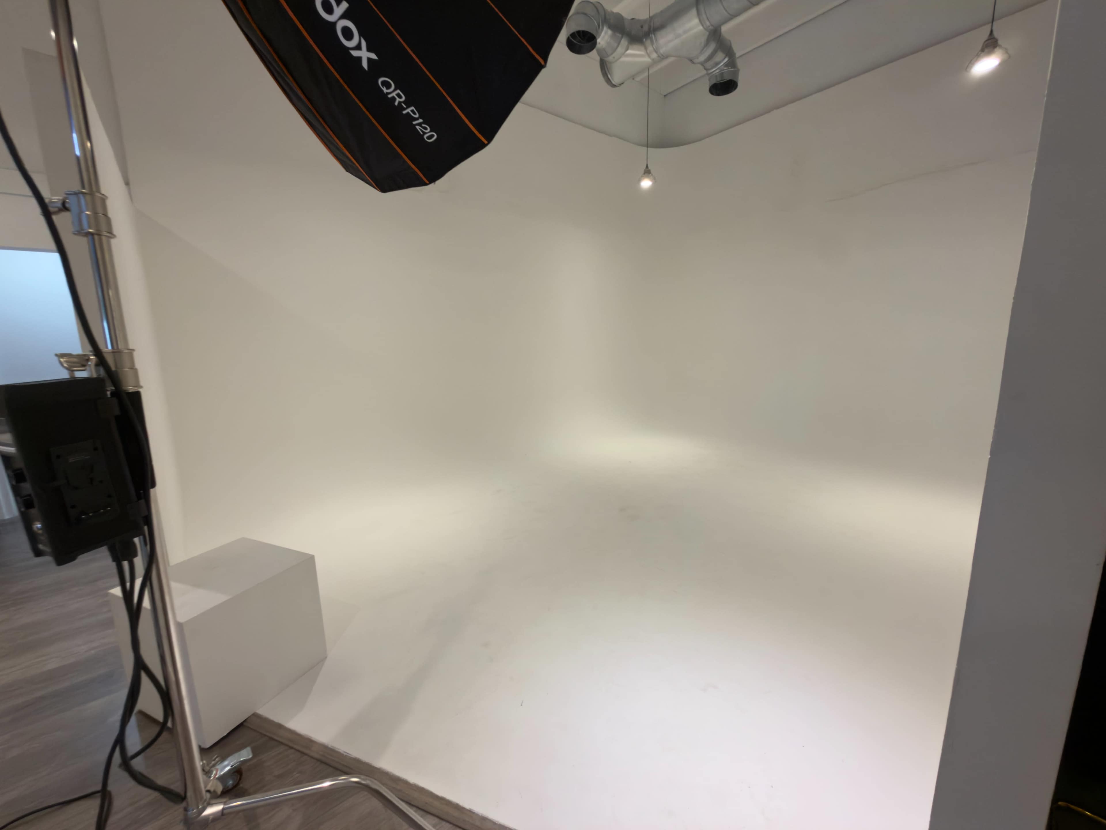 The image shows a spacious photography studio with a clean white backdrop and an overhead lighting setup.