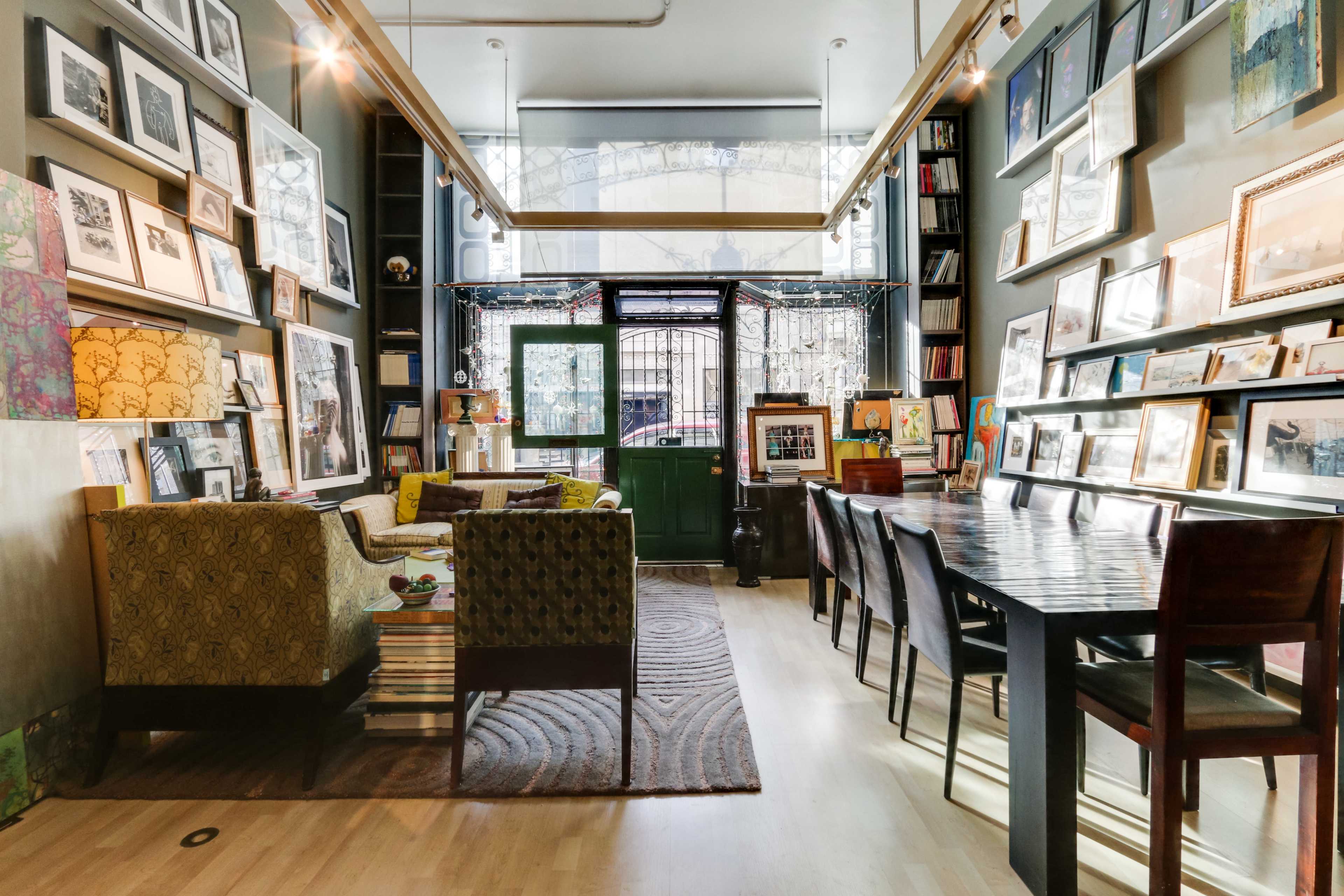 A cozy interior of a cafe or gallery, featuring an assortment of framed artwork on the walls, comfortable seating, and a long dining table.