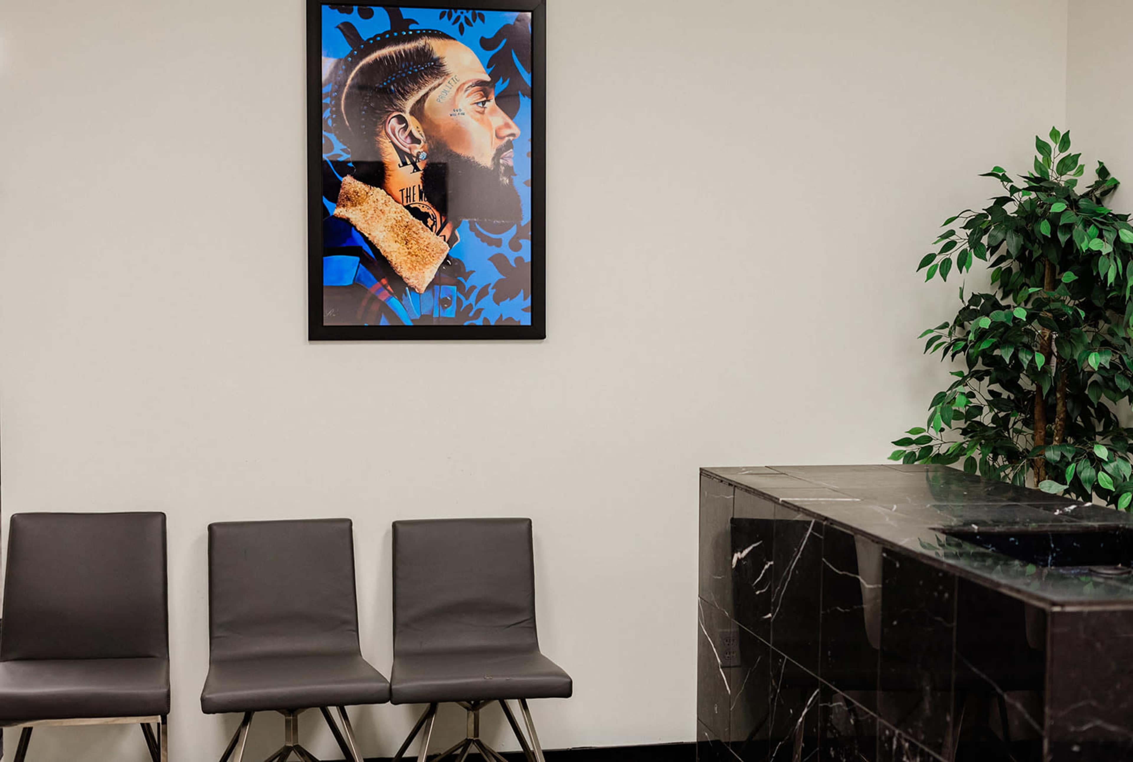 A waiting area with three black chairs, a dark marble reception desk, and a framed portrait of a man on the wall.