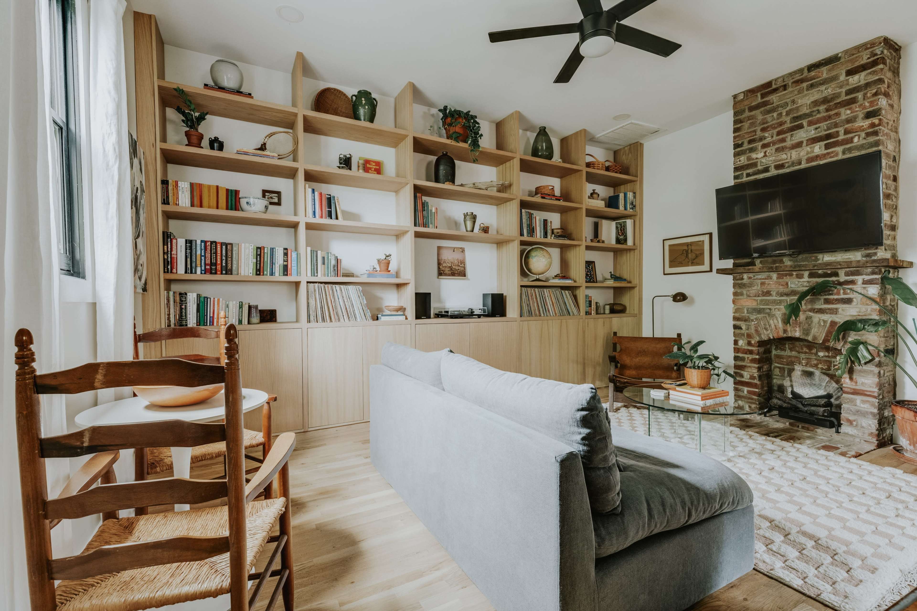 A cozy living room features a bookshelf filled with books, a television mounted on the wall, and a comfortable seating area with a coffee table.