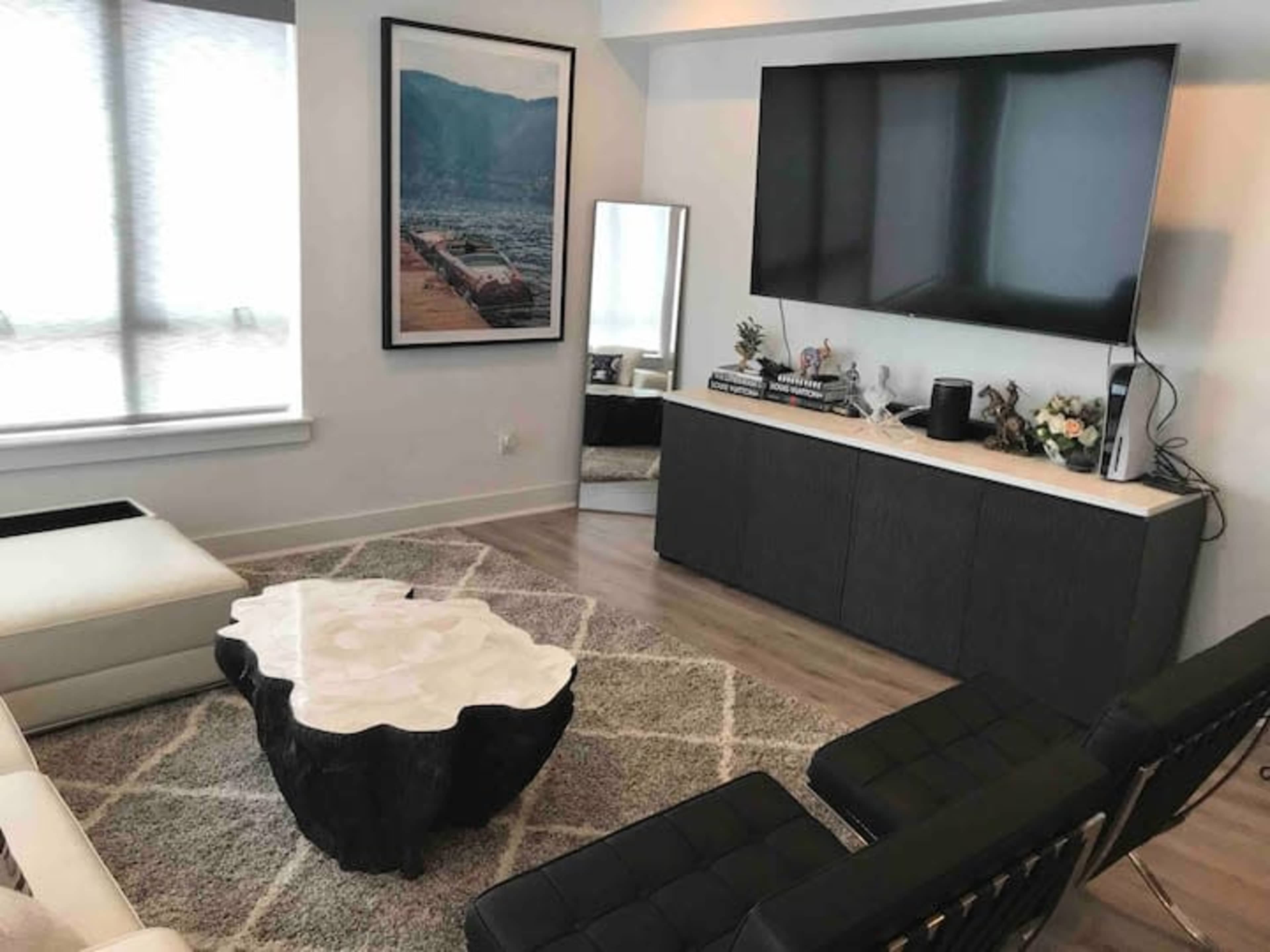 A modern living room with a large television mounted on the wall, a decorative coffee table in the center, and seating arranged around a plush area rug.