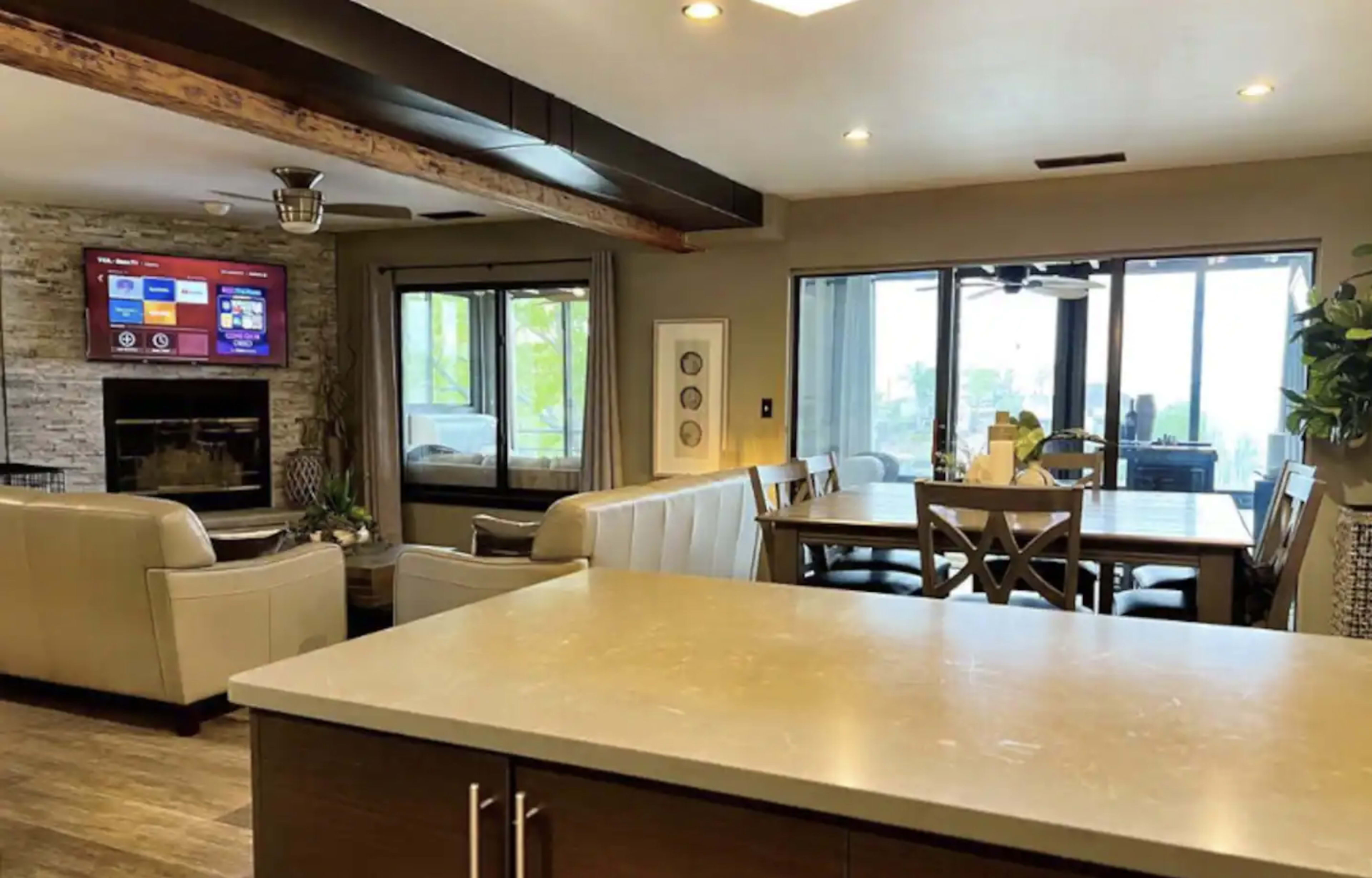 A modern, open-concept living and dining area features a fireplace, large windows, and a seating arrangement with a view of the dining table.