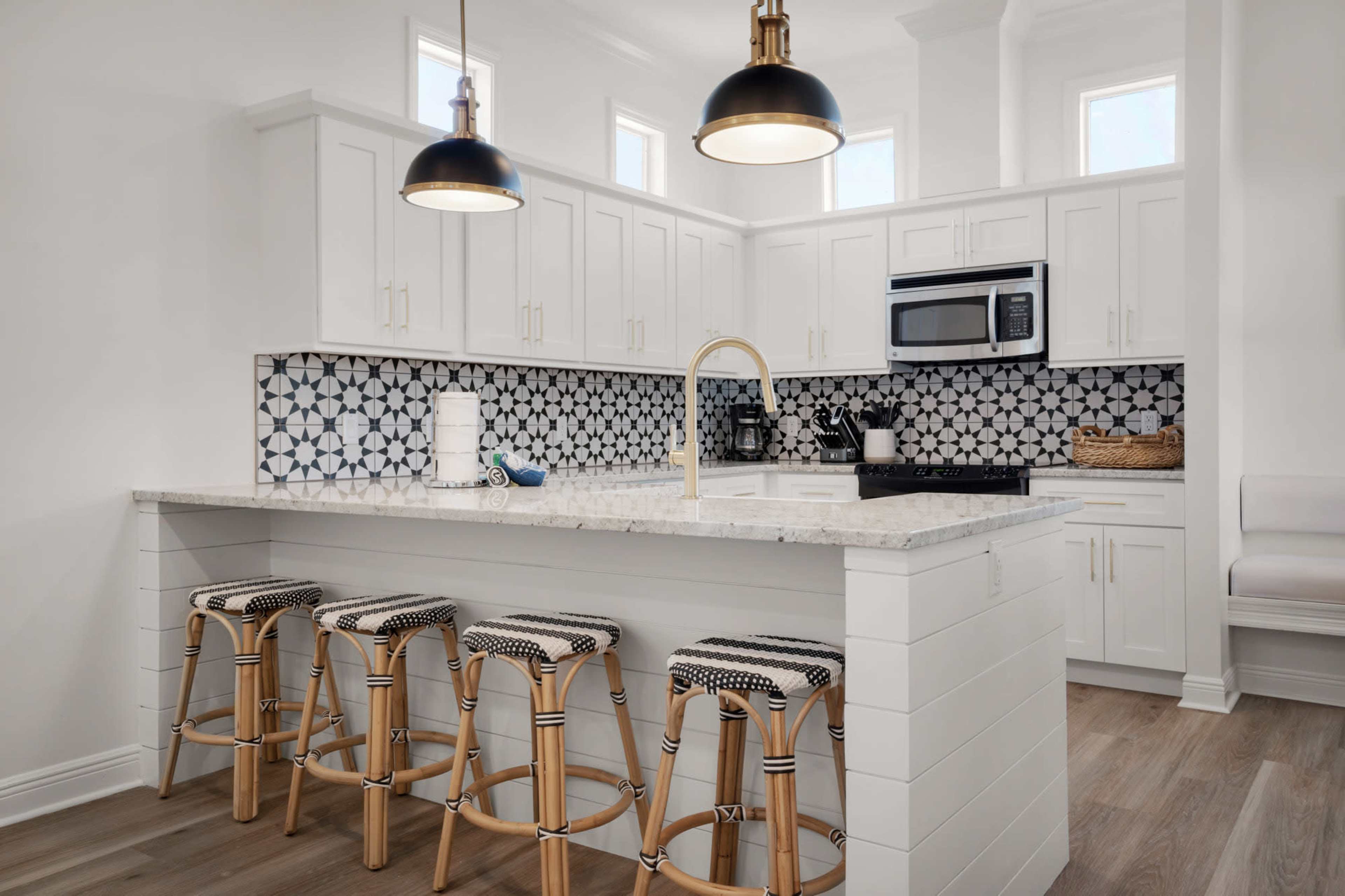 A modern kitchen with white cabinetry, a patterned backsplash, and a central island with four stool seats.