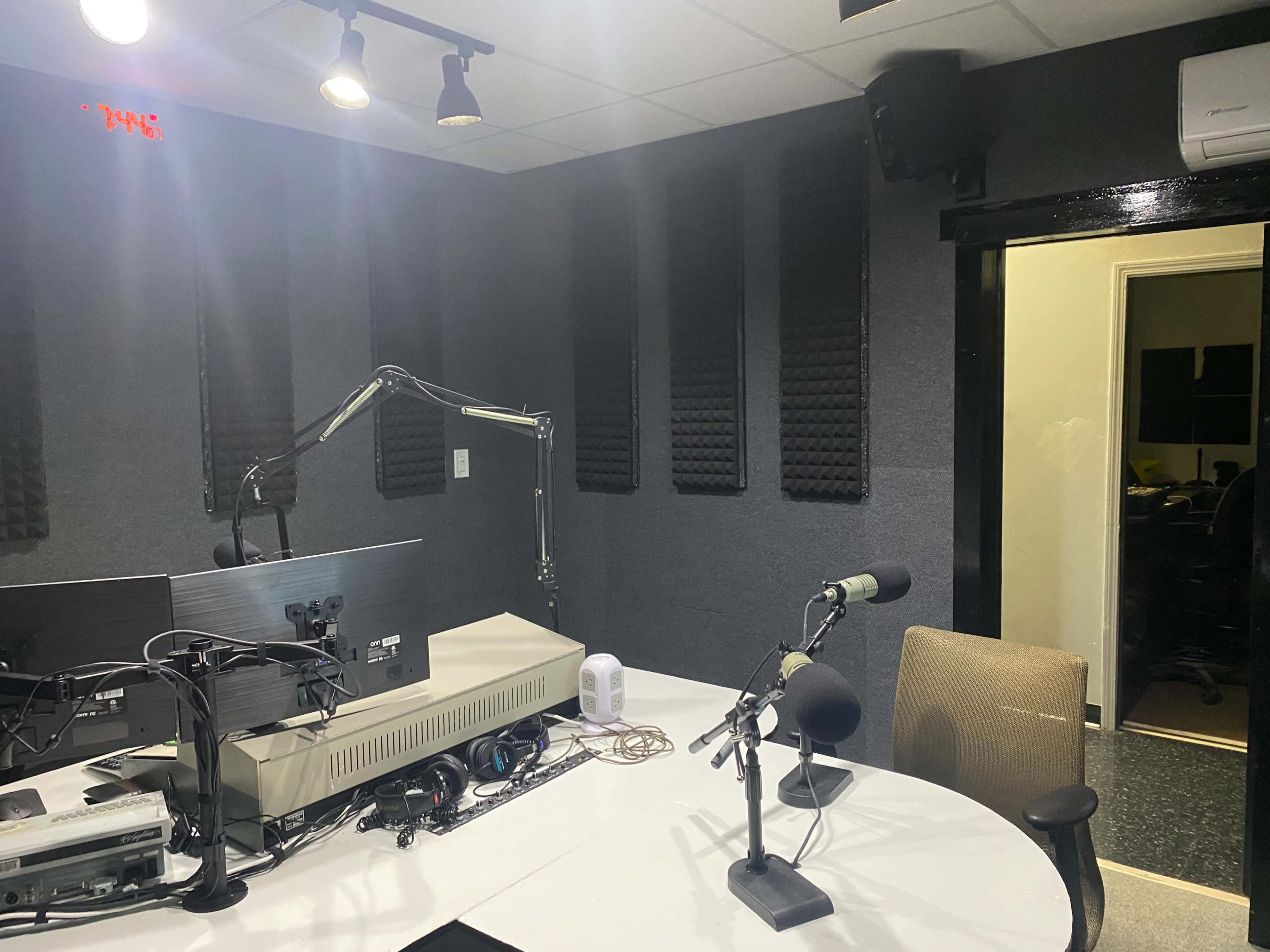 A radio studio with soundproof walls, a microphone setup, and a desk with monitors.