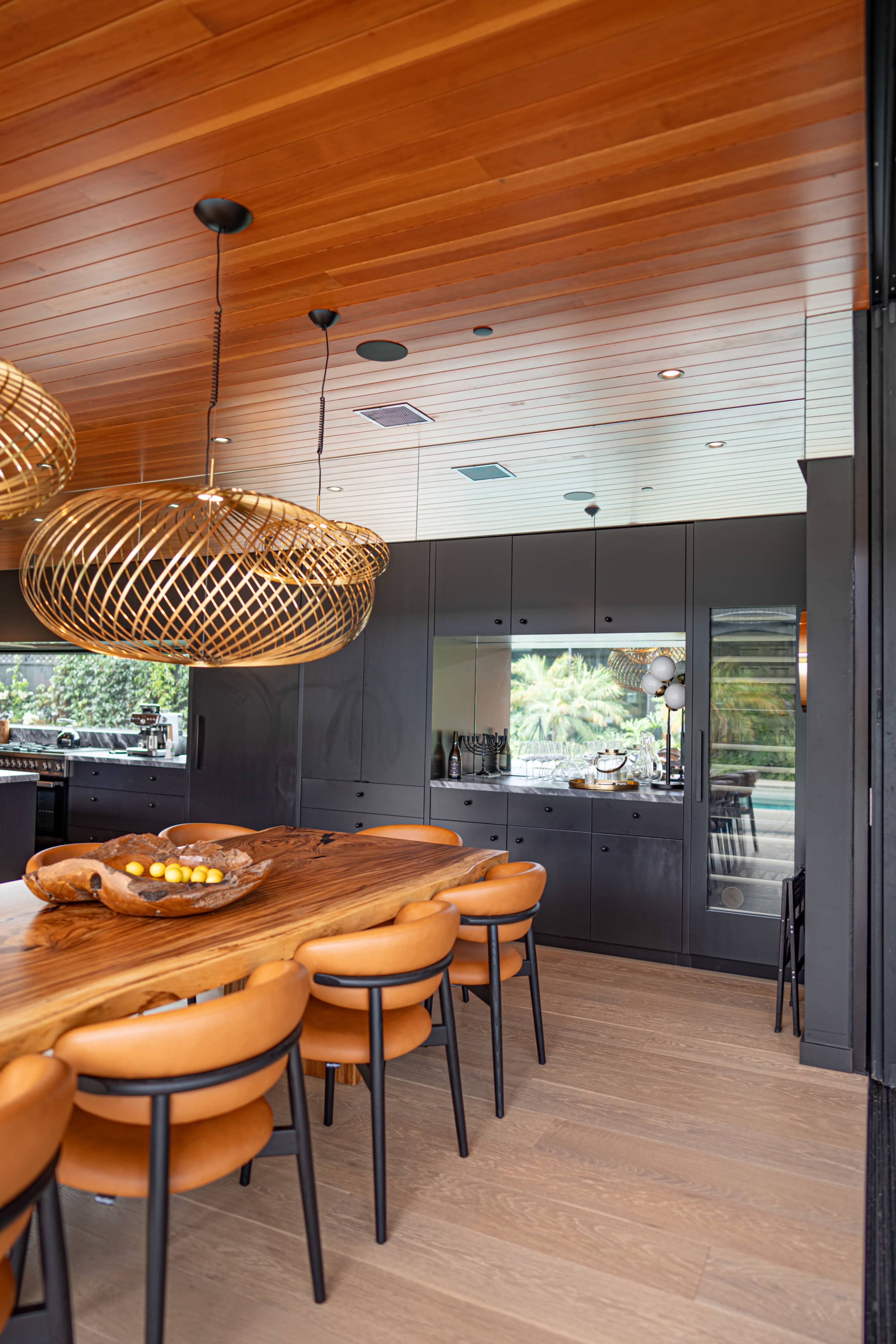 A contemporary dining area features a large wooden table surrounded by black chairs and illuminated by woven pendant lights.