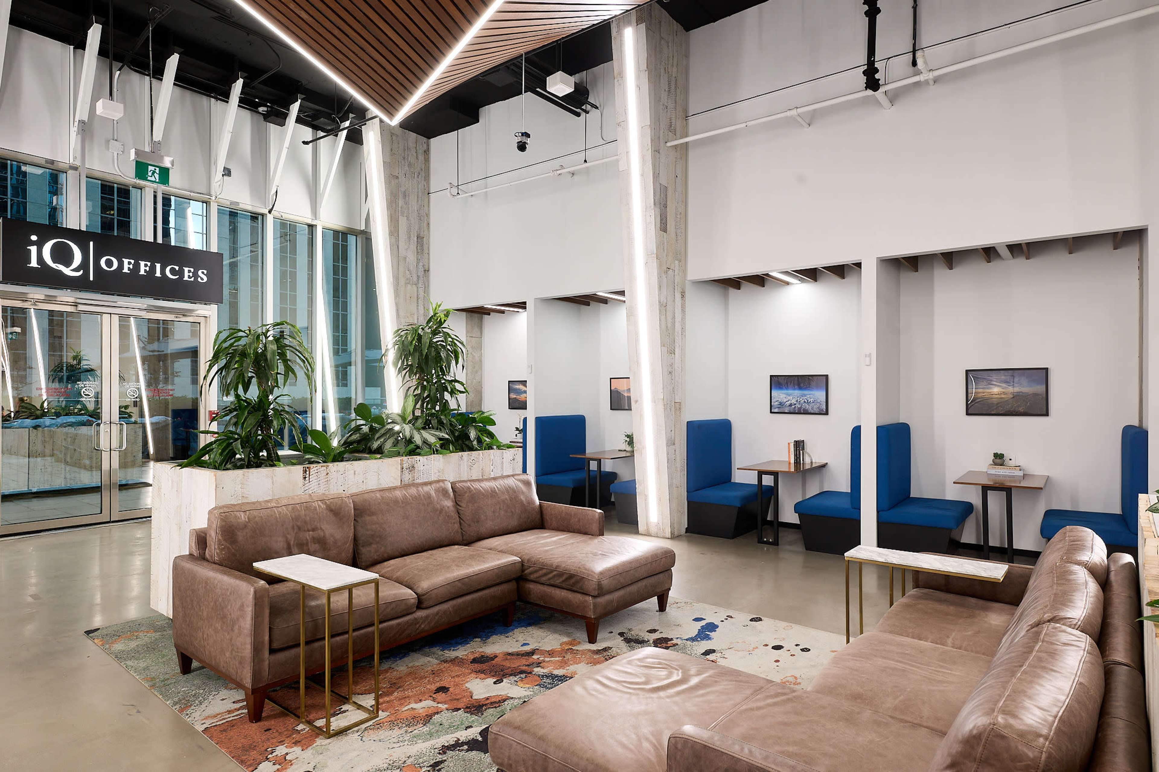 The image shows a modern office space with a seating area featuring a brown leather couch, a patterned rug, and blue booths against the wall.