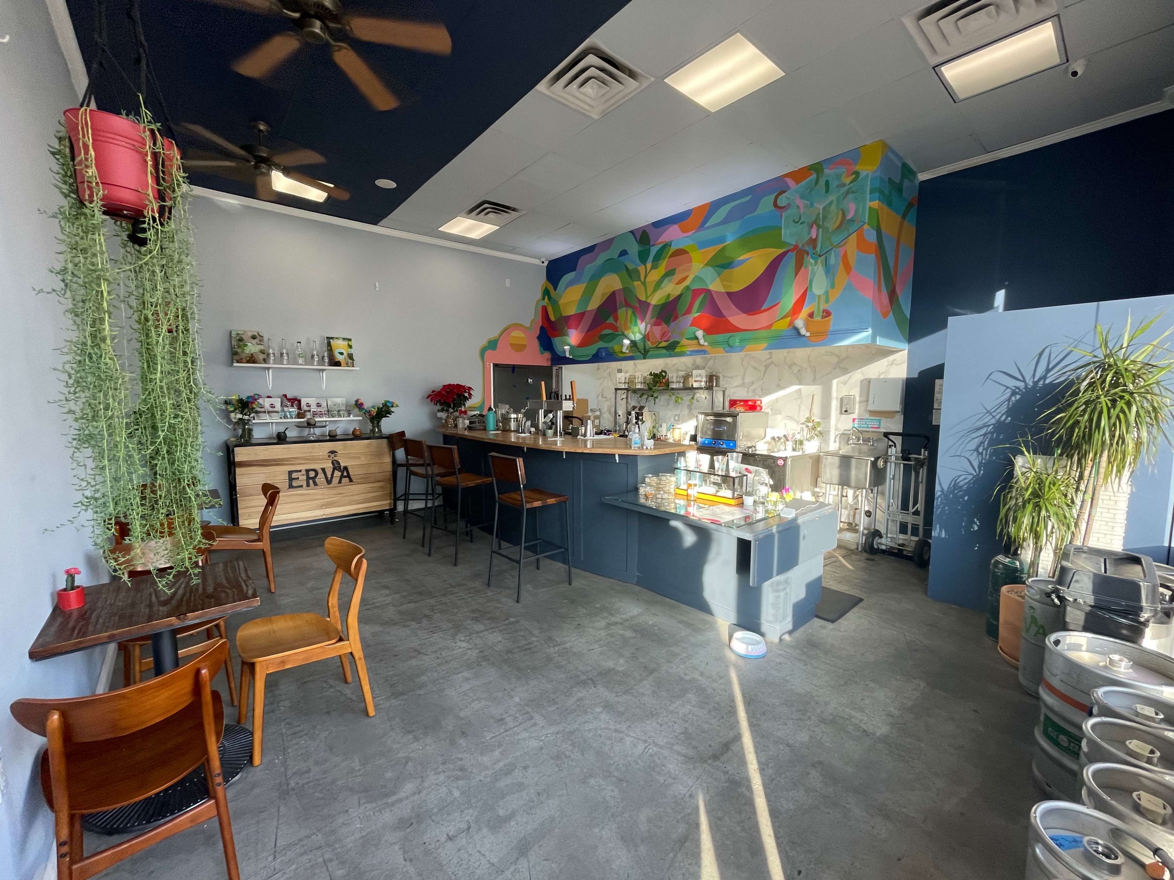 A cafe interior with a colorful mural, wooden furniture, and an open bar area behind a counter.