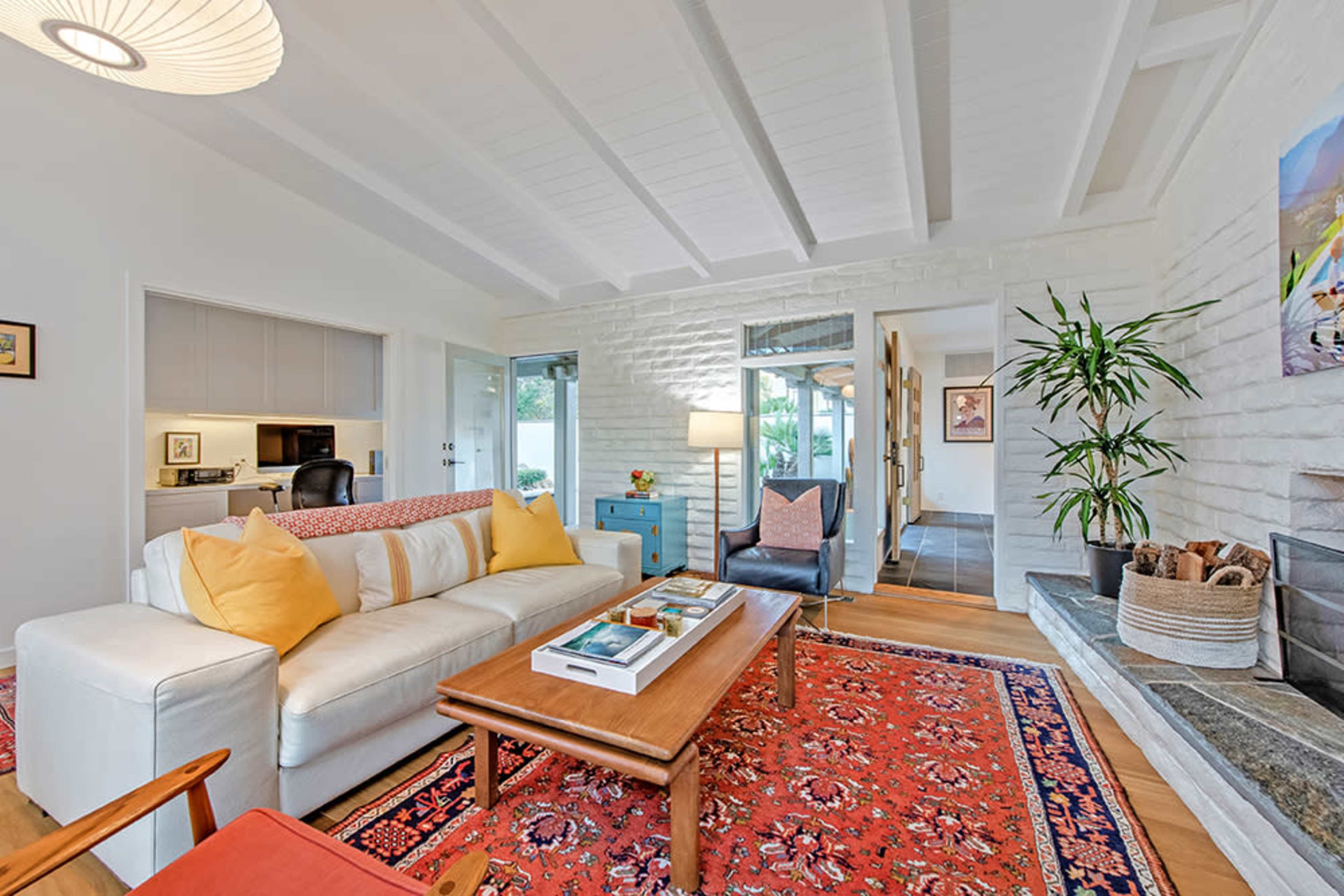 The image shows a modern living room featuring a white sofa with yellow pillows, a wooden coffee table, and a decorative rug on the floor.