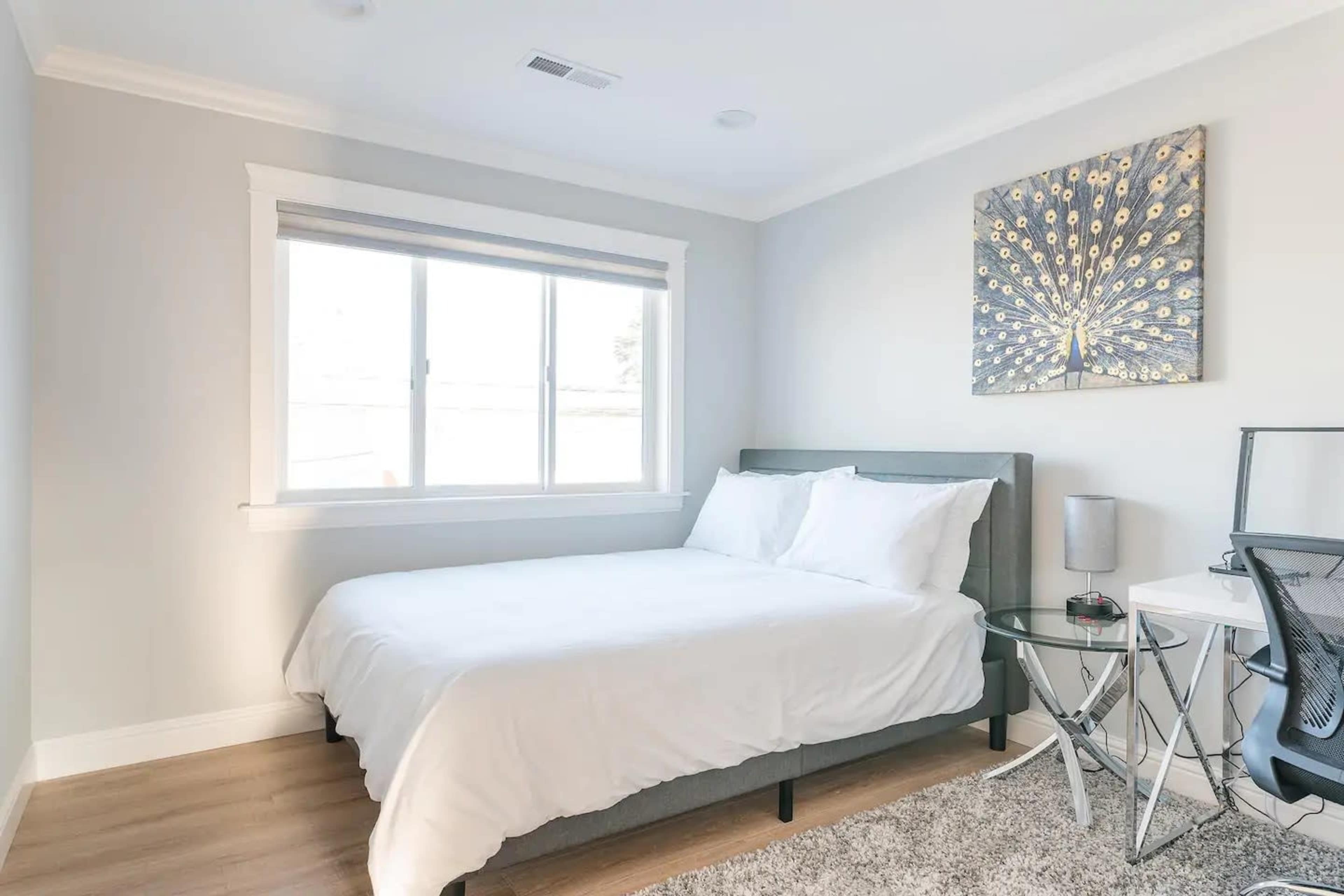 A minimalist bedroom with a double bed, a small desk, and a window featuring natural light.