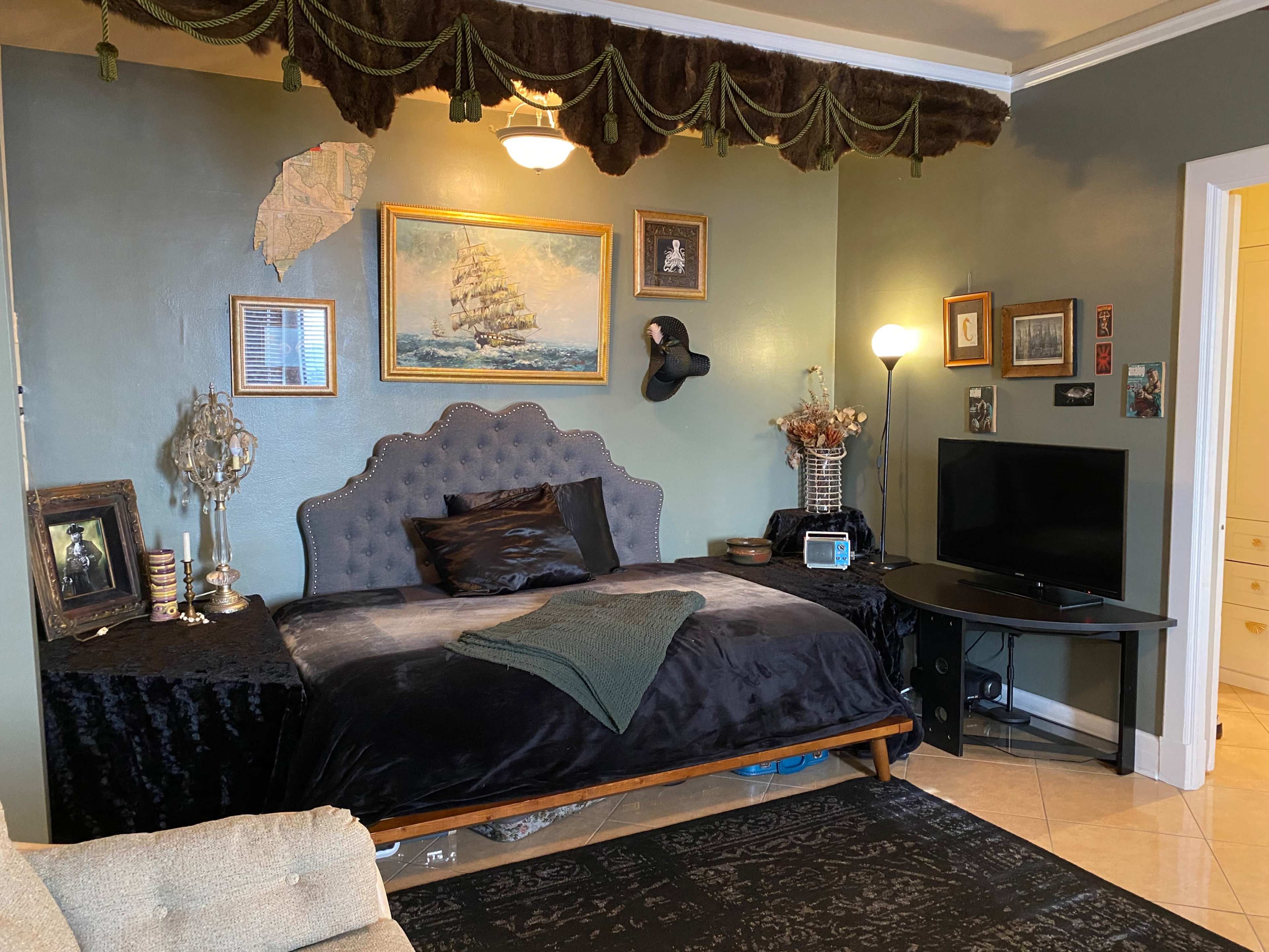 The image shows a cozy bedroom with a plush bed, decorative wall art, and a television set against an accent wall.