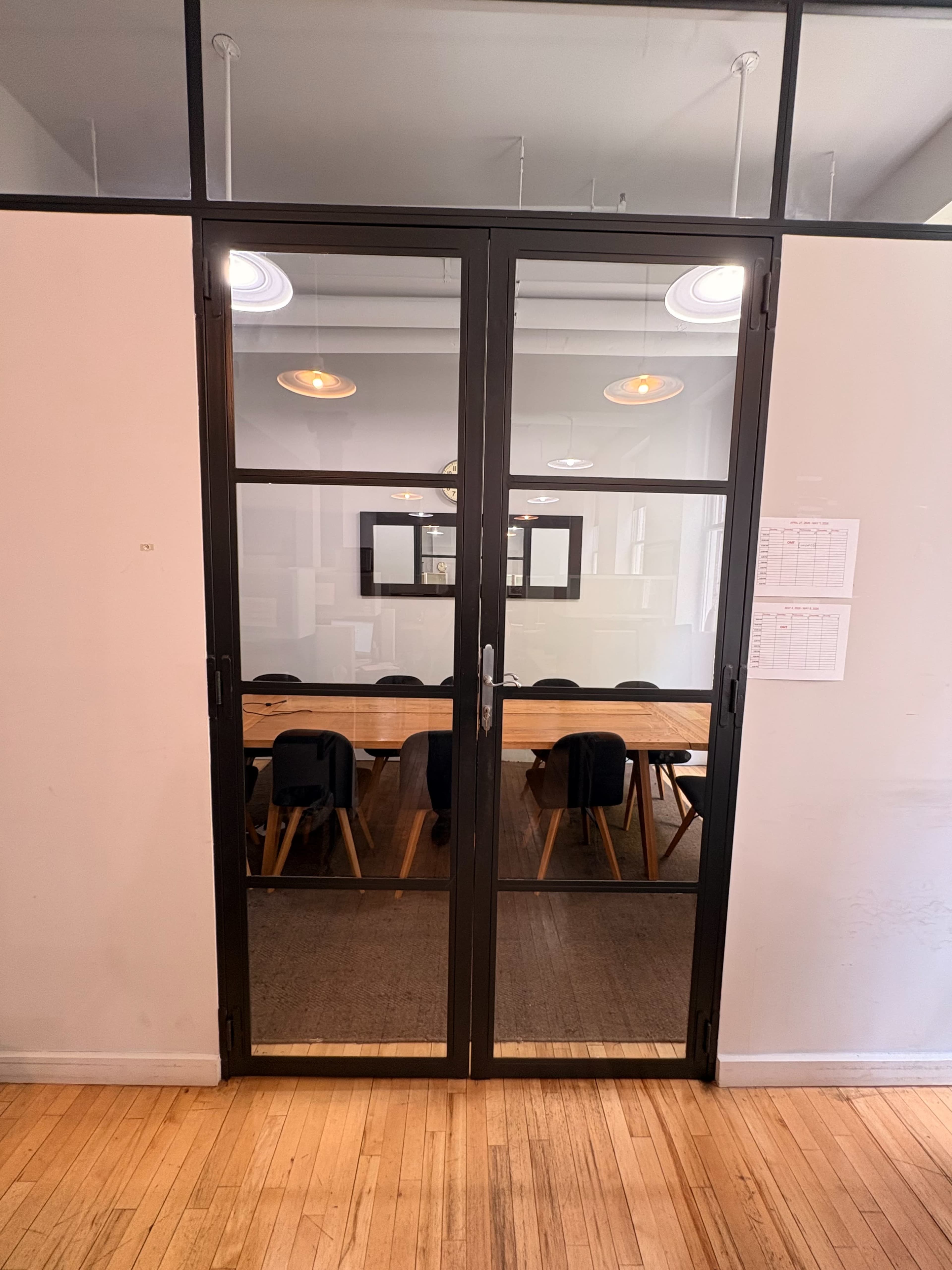 A set of glass double doors leads into a conference room with a long wooden table and chairs positioned around it.