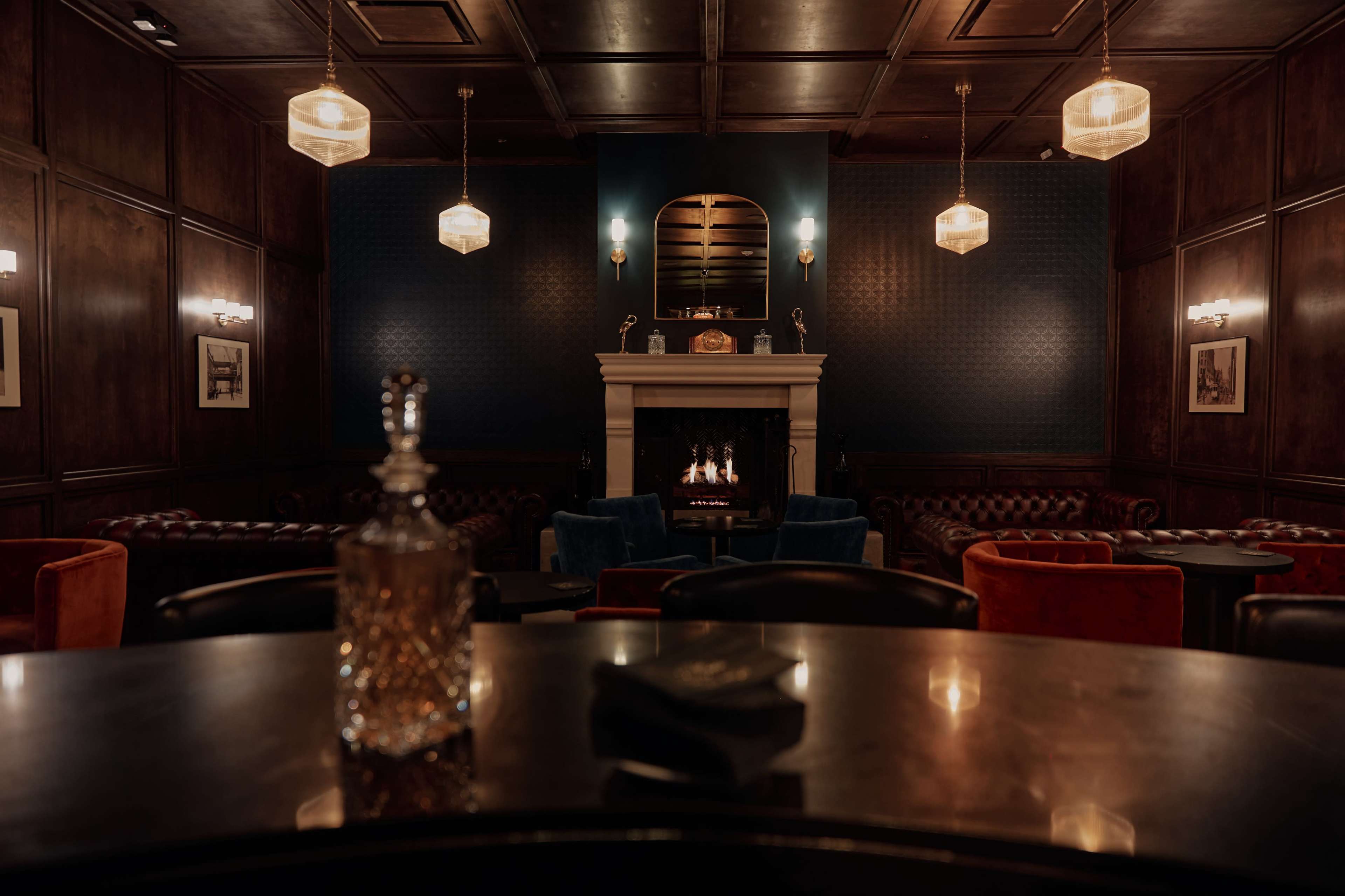 A dimly lit lounge features wooden paneling, a fireplace, and plush seating arrangements with decorative lighting above.