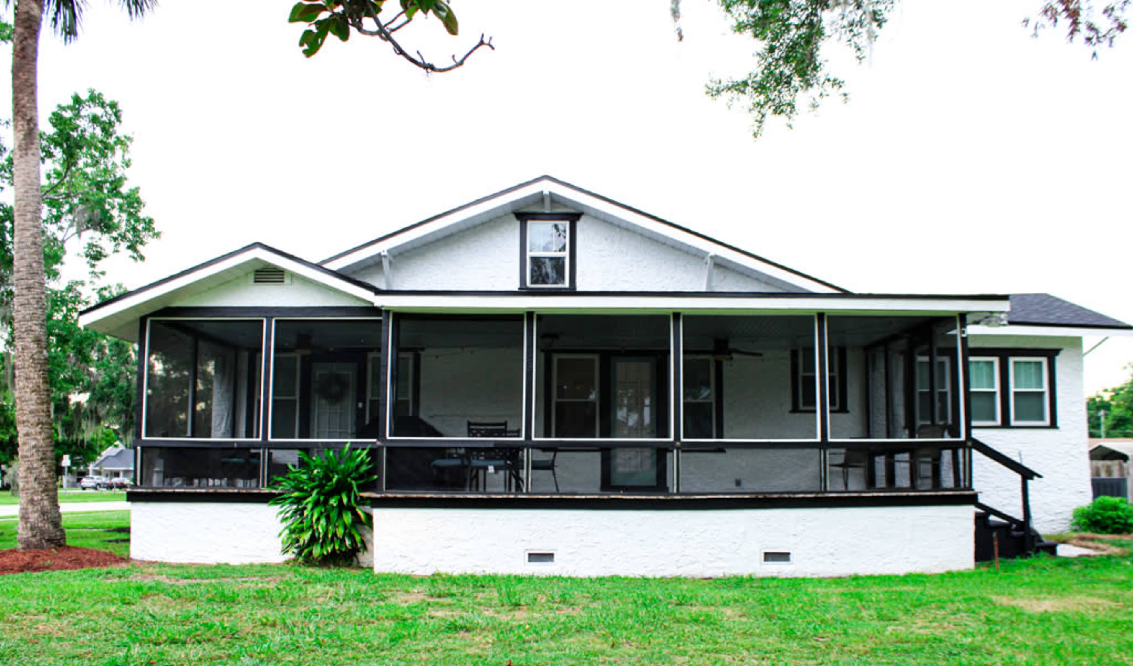 The image shows a single-story house with a spacious screened porch and a grassy yard.
