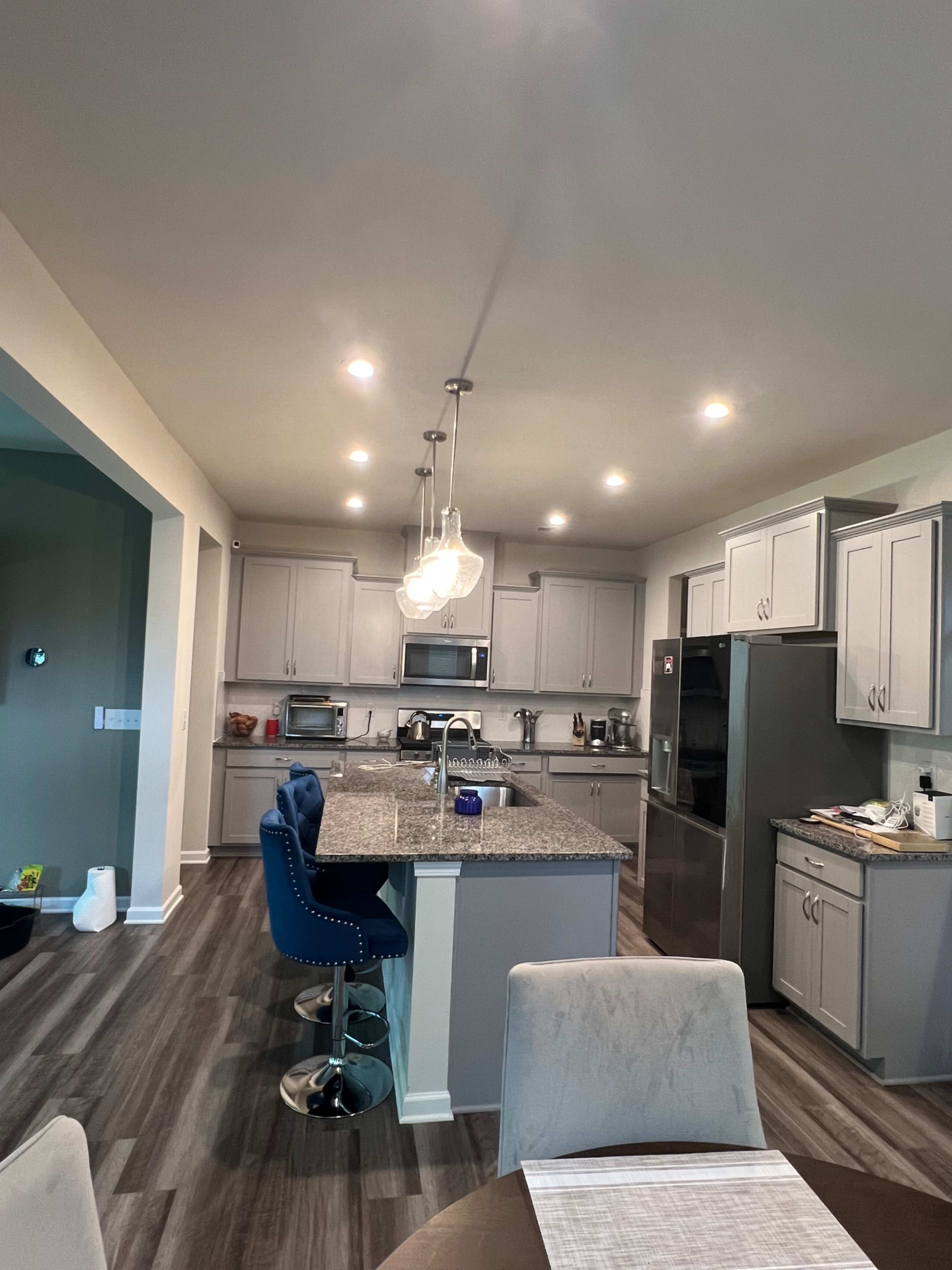 A modern kitchen with gray cabinets, a large central island, and pendant lighting, featuring stainless steel appliances and a dining area in the foreground.