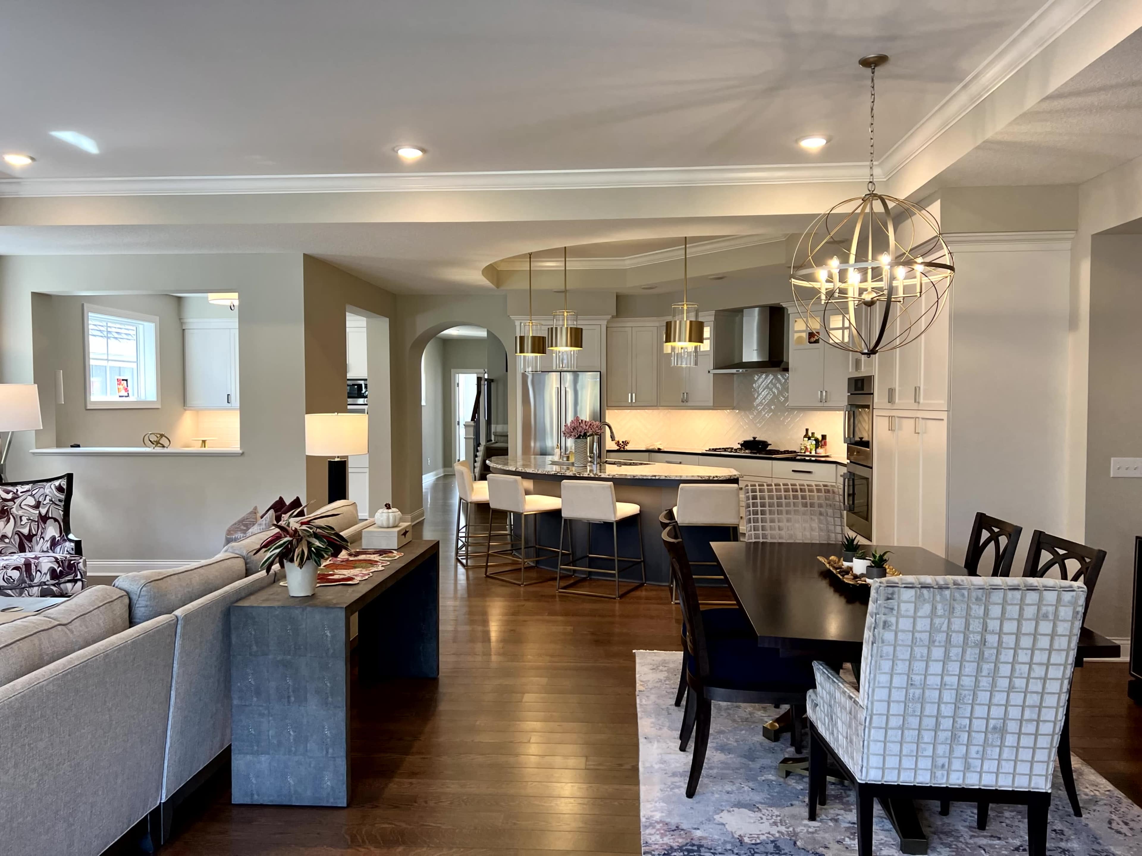 The image shows a modern open-concept kitchen and dining area with a large dining table, bar seating, and contemporary lighting fixtures.